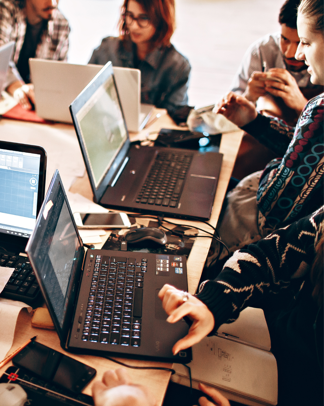 People working on laptops around a table with multiple electronic devices.
