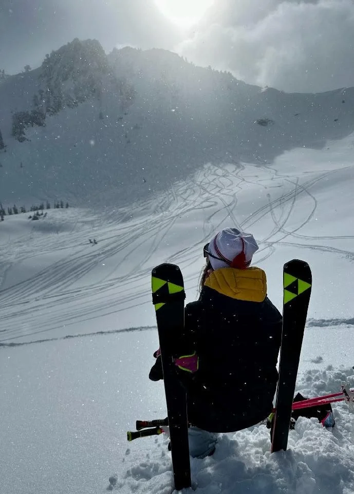 Ivey resting in deep snow after a day of backcountry skiing, surrounded by alpine peaks and winter stillness—capturing the quiet side of adventure.