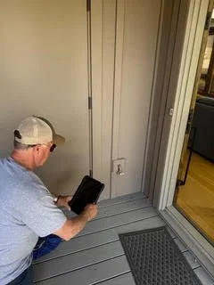 A man wearing a cap and gray shirt sitting on a porch, looking at a tablet.