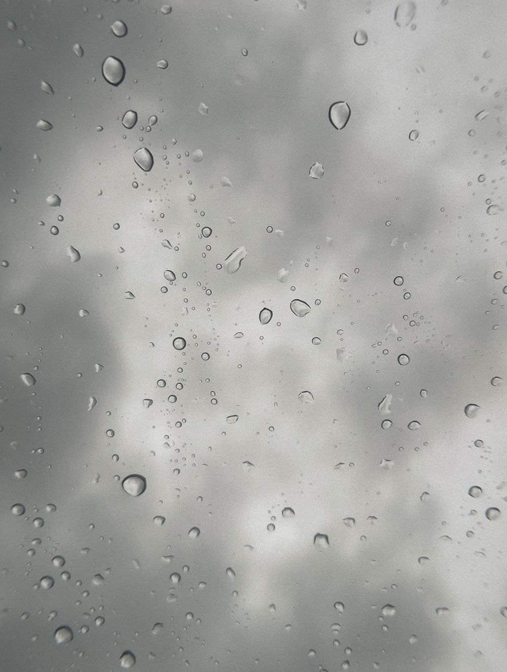 Rain droplets on a glass window with a cloudy sky in the background.