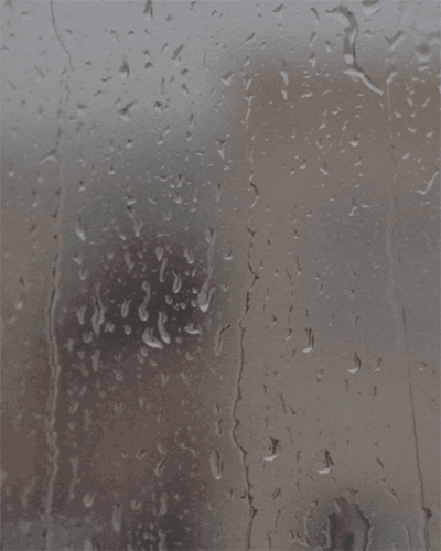 Rain-covered window with blurred view of a person and building outside.