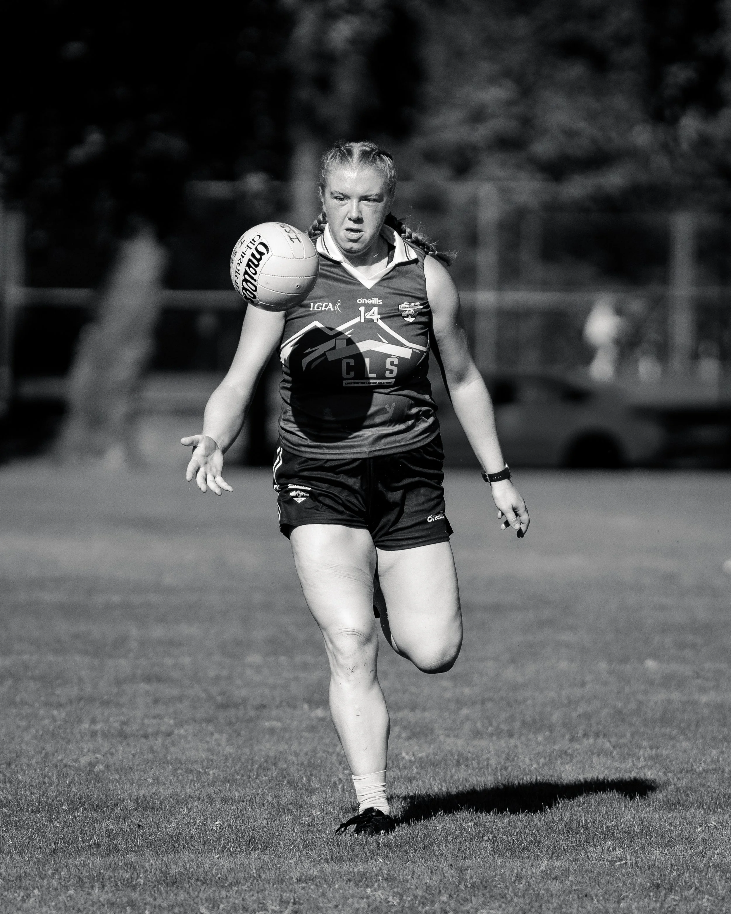 A female athlete is running on a field while balancing a football in her hand.