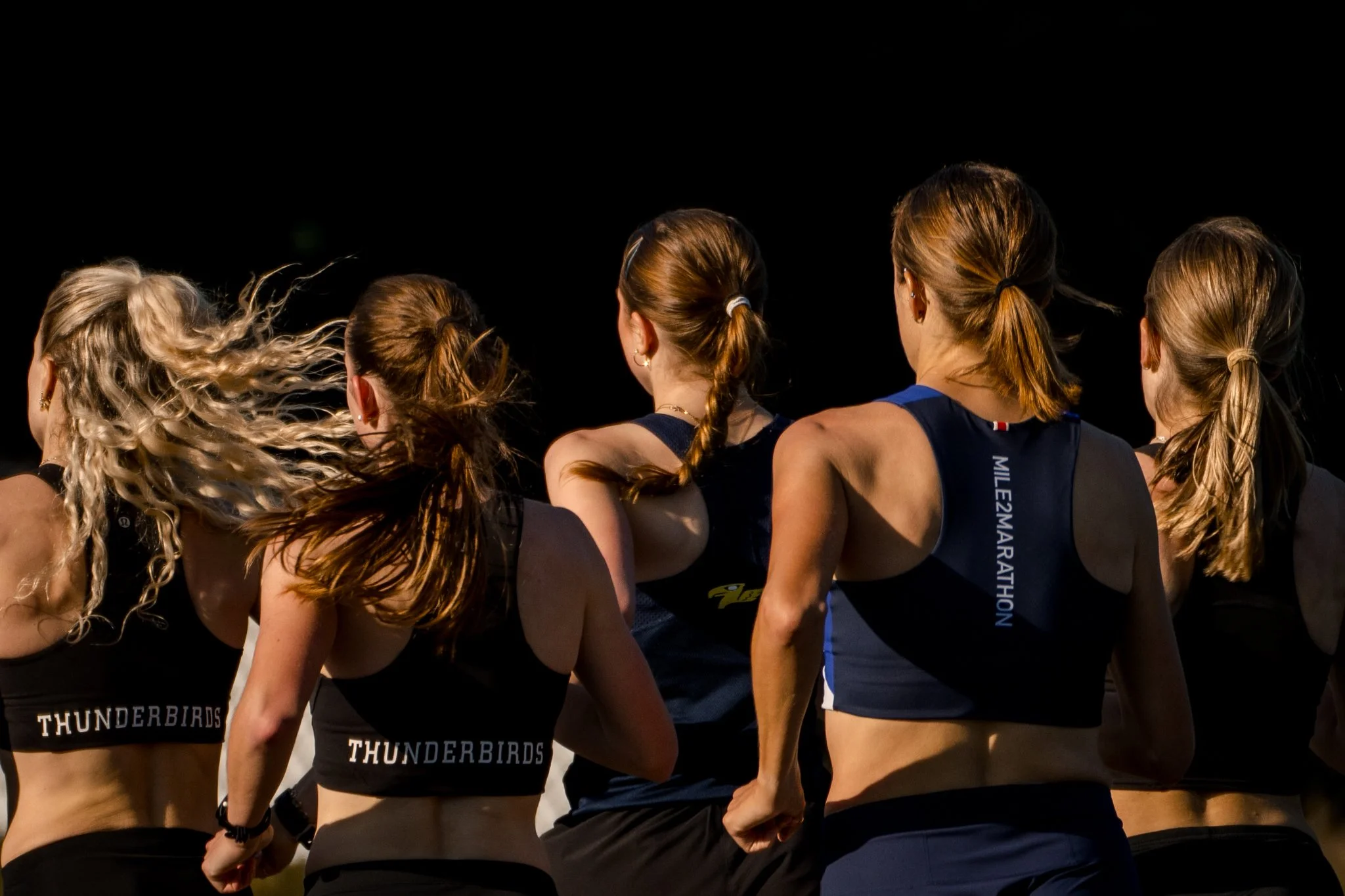 Group of female runners, seen from behind, participating in a race at night, wearing athletic gear.
