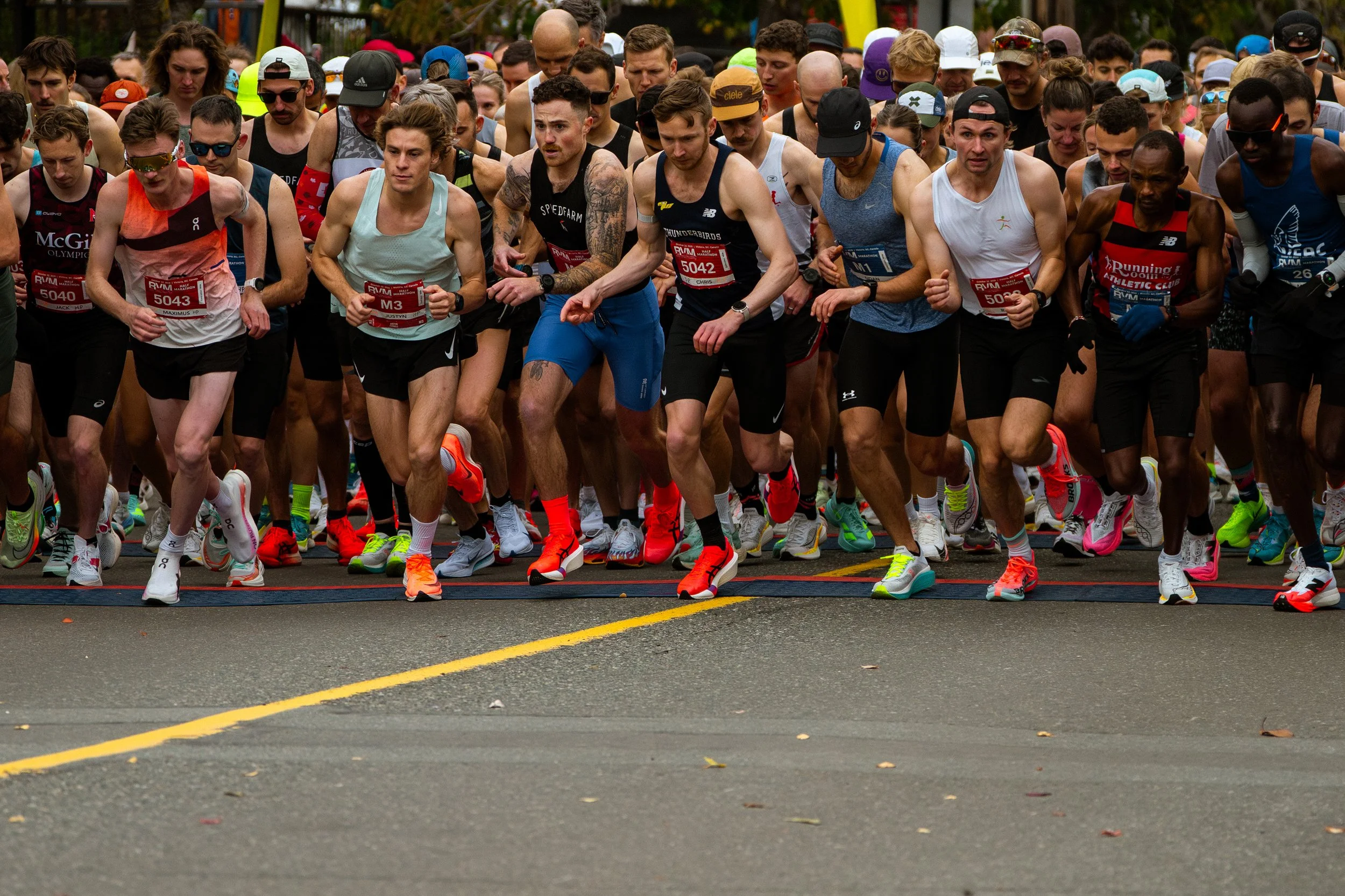 Start of a marathon race with many runners in athletic gear, some wearing sunglasses and hats, with focused expressions as they begin to run.
