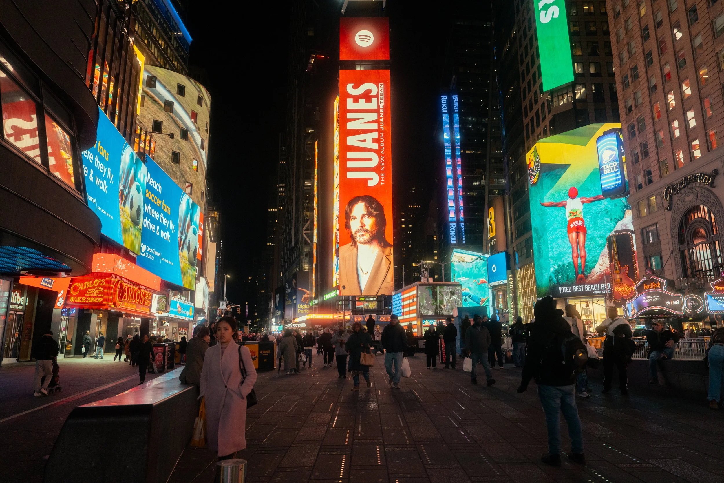 Nighttime scene in Times Square, New York City, with bright digital billboards and advertisements, crowds of people, and illuminated signs.