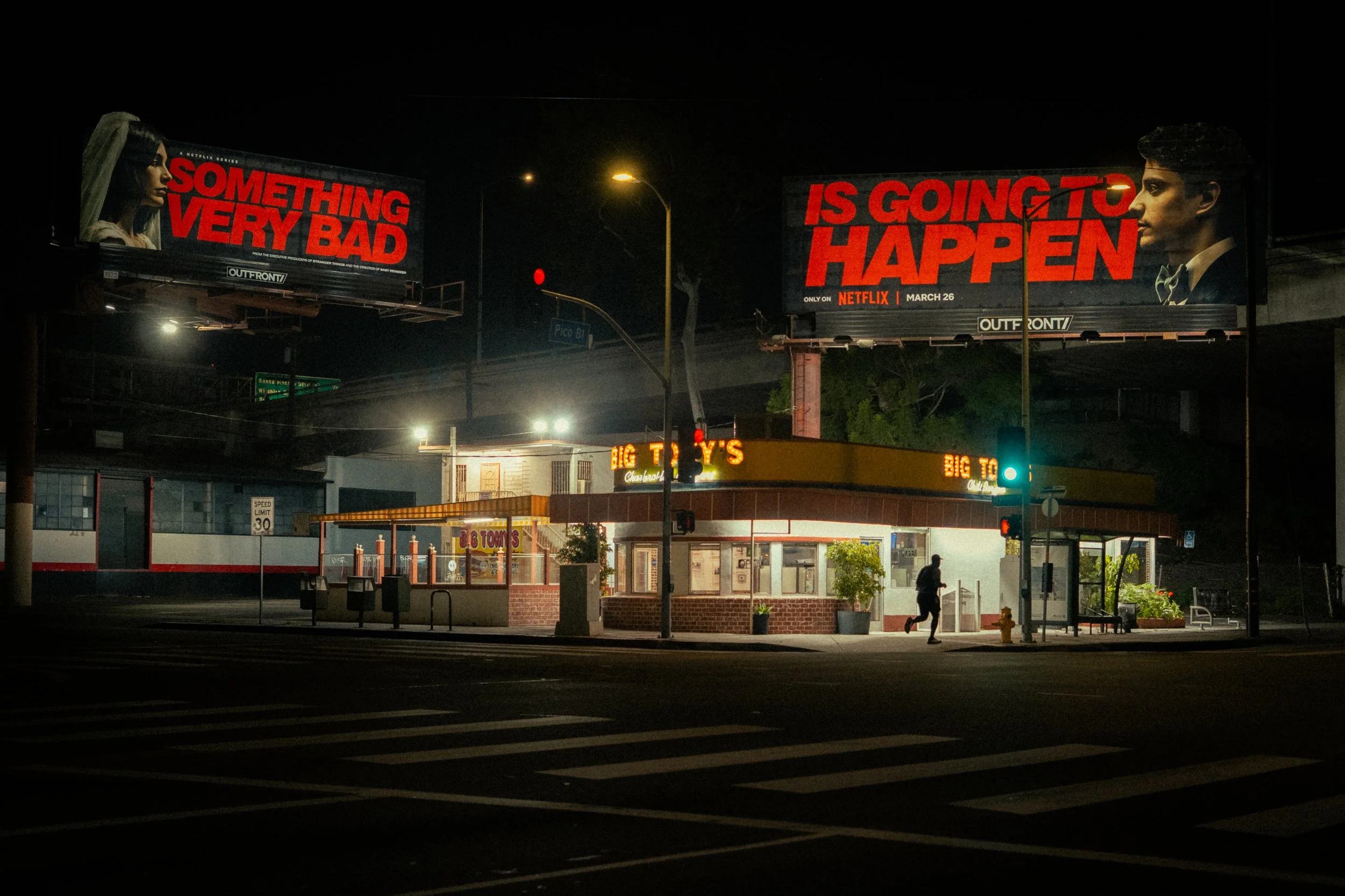 Nighttime city scene with two billboards displaying text, a person running across a crosswalk, and a fast-food restaurant named Big T's in the background.