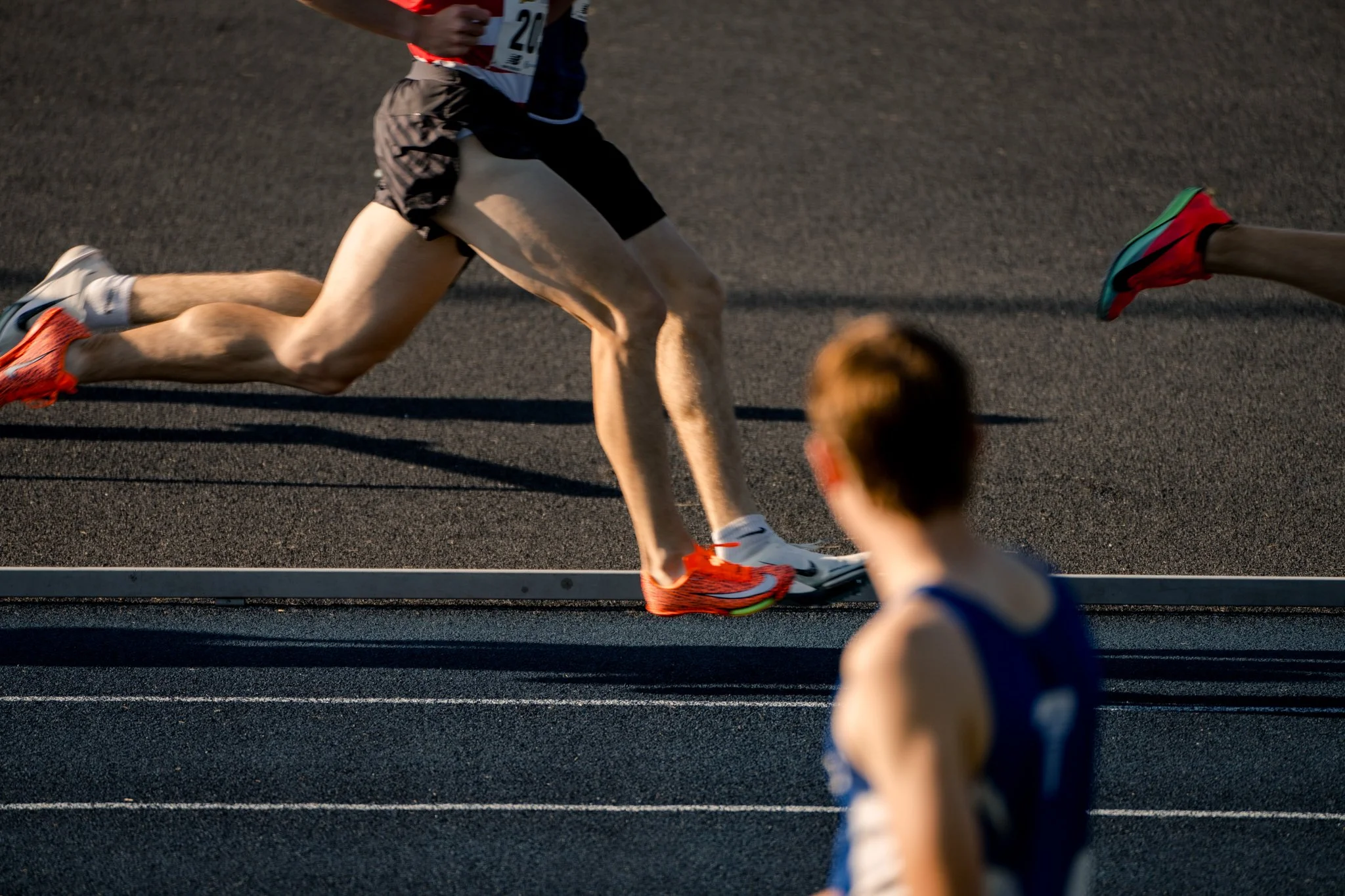 Close-up of runners' legs competing in a race on a track, with focus on the person in the foreground wearing orange shoes.