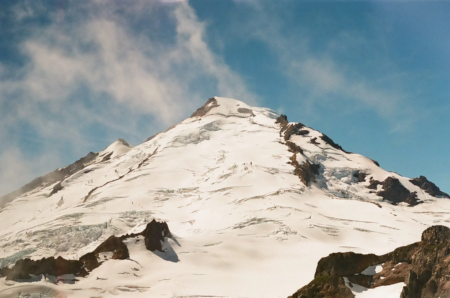 Snow-covered mountain with rocky outcrops and a cloudy sky.
