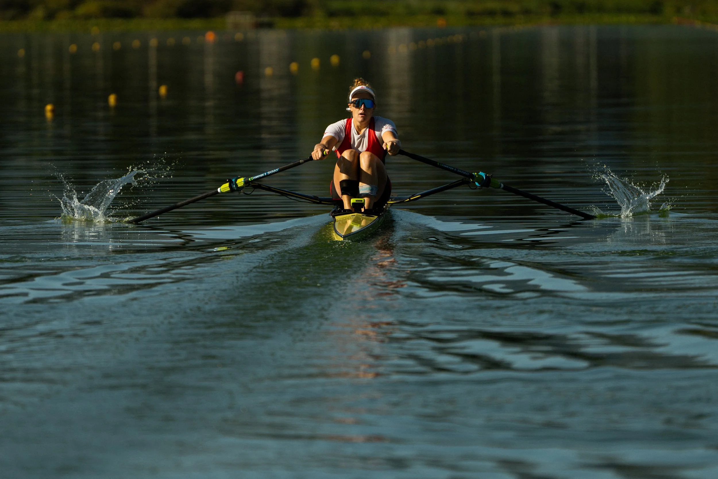 A woman wearing sunglasses, a white visor, and athletic clothing cross-country skiing on a calm lake during the daytime.