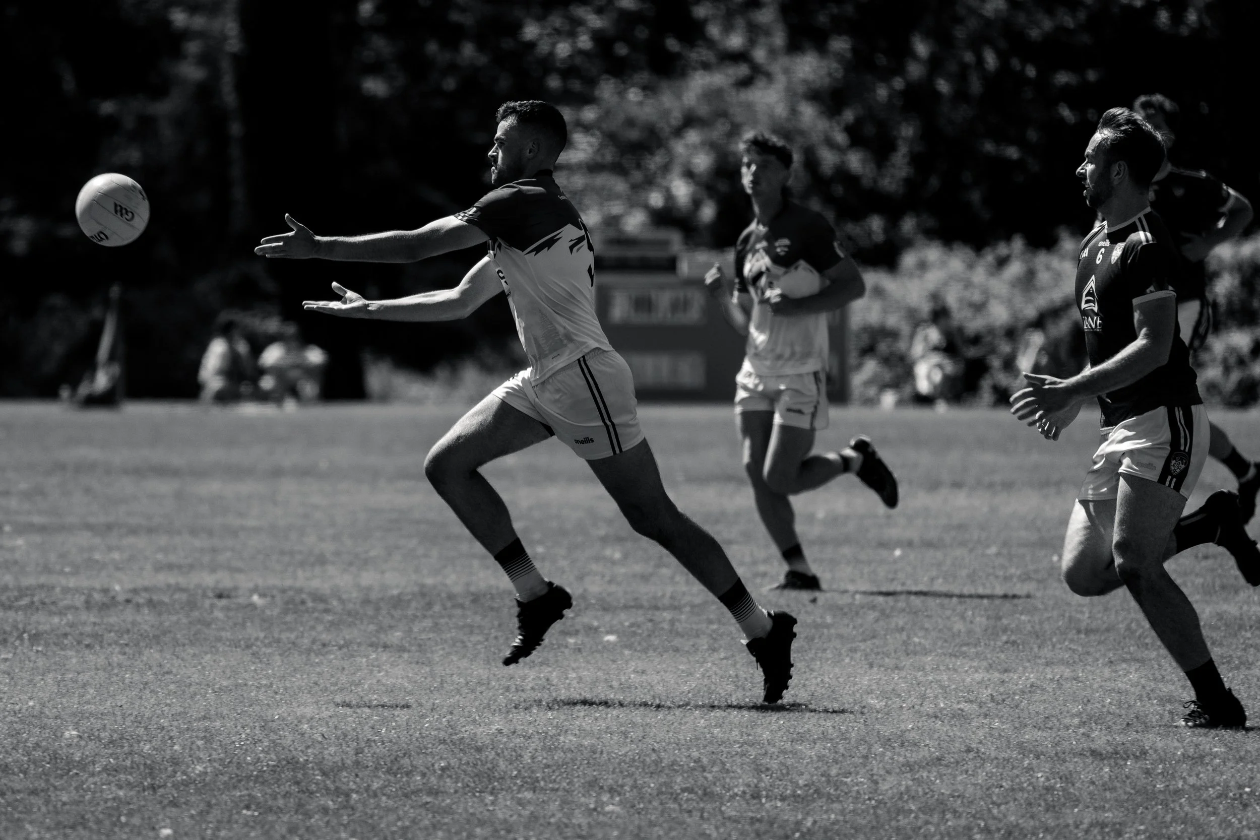 Sports players in athletic uniforms running and reaching for a rugby ball on the field, black and white photo.