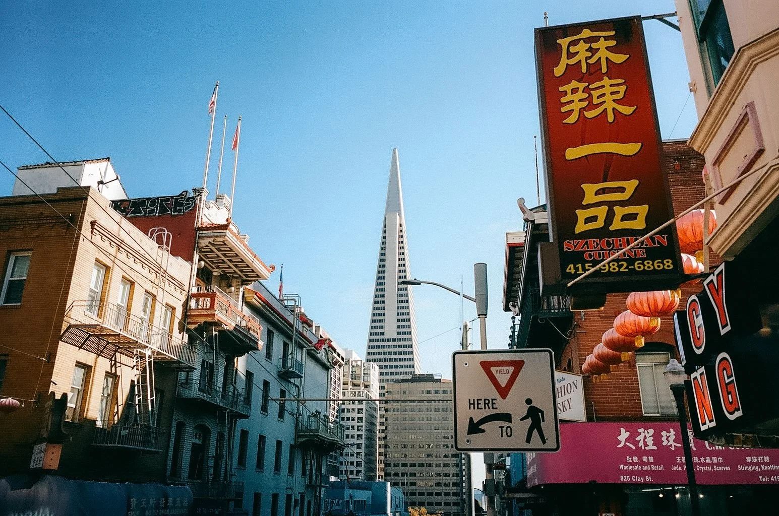 View of Chinatown with colorful storefronts, Asian signs, paper lanterns, and the Transamerica Pyramid skyscraper in San Francisco in the background.