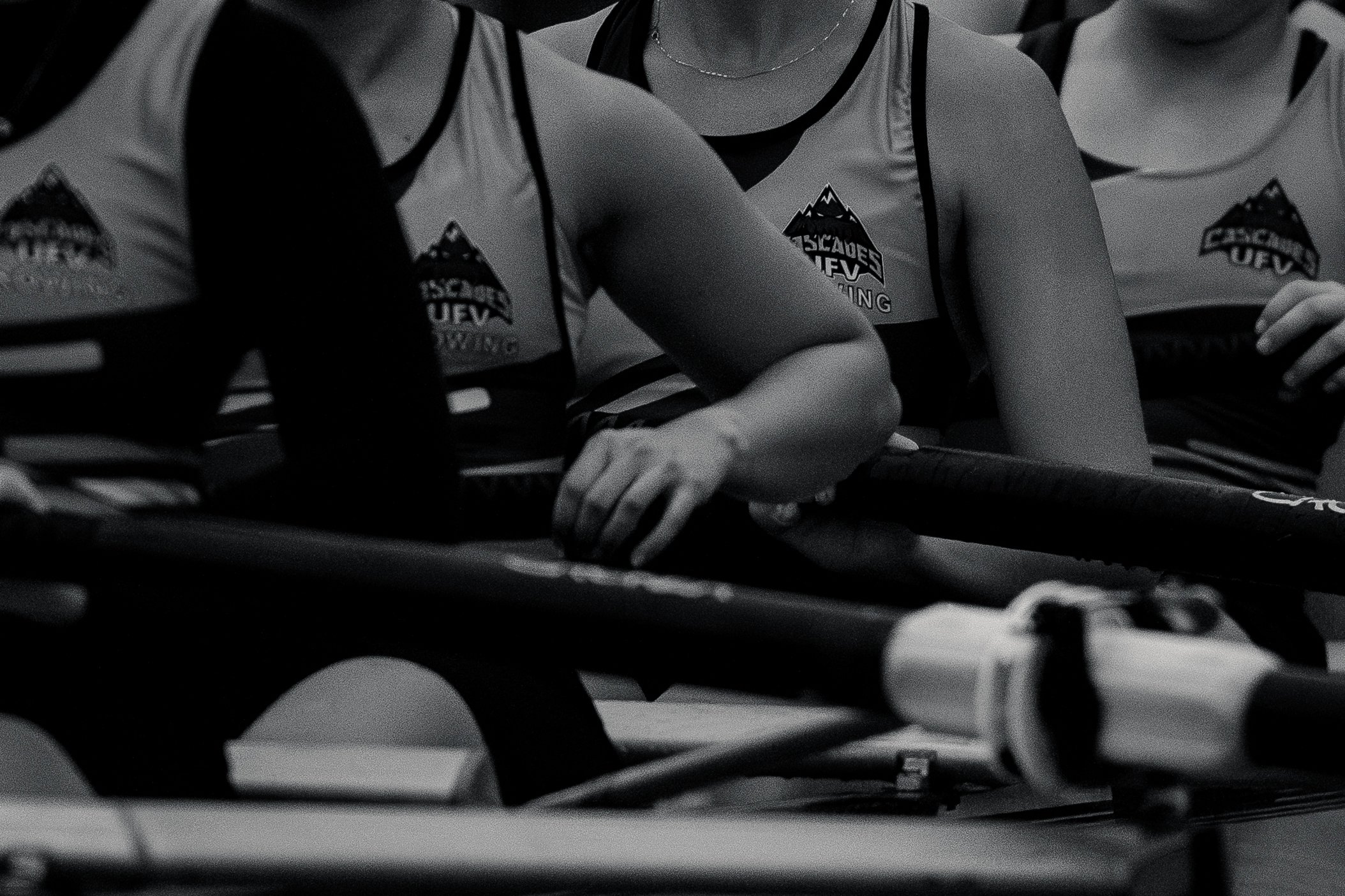 Close-up of female rowers in a boat wearing matching jerseys with a mountain logo, preparing for a race.
