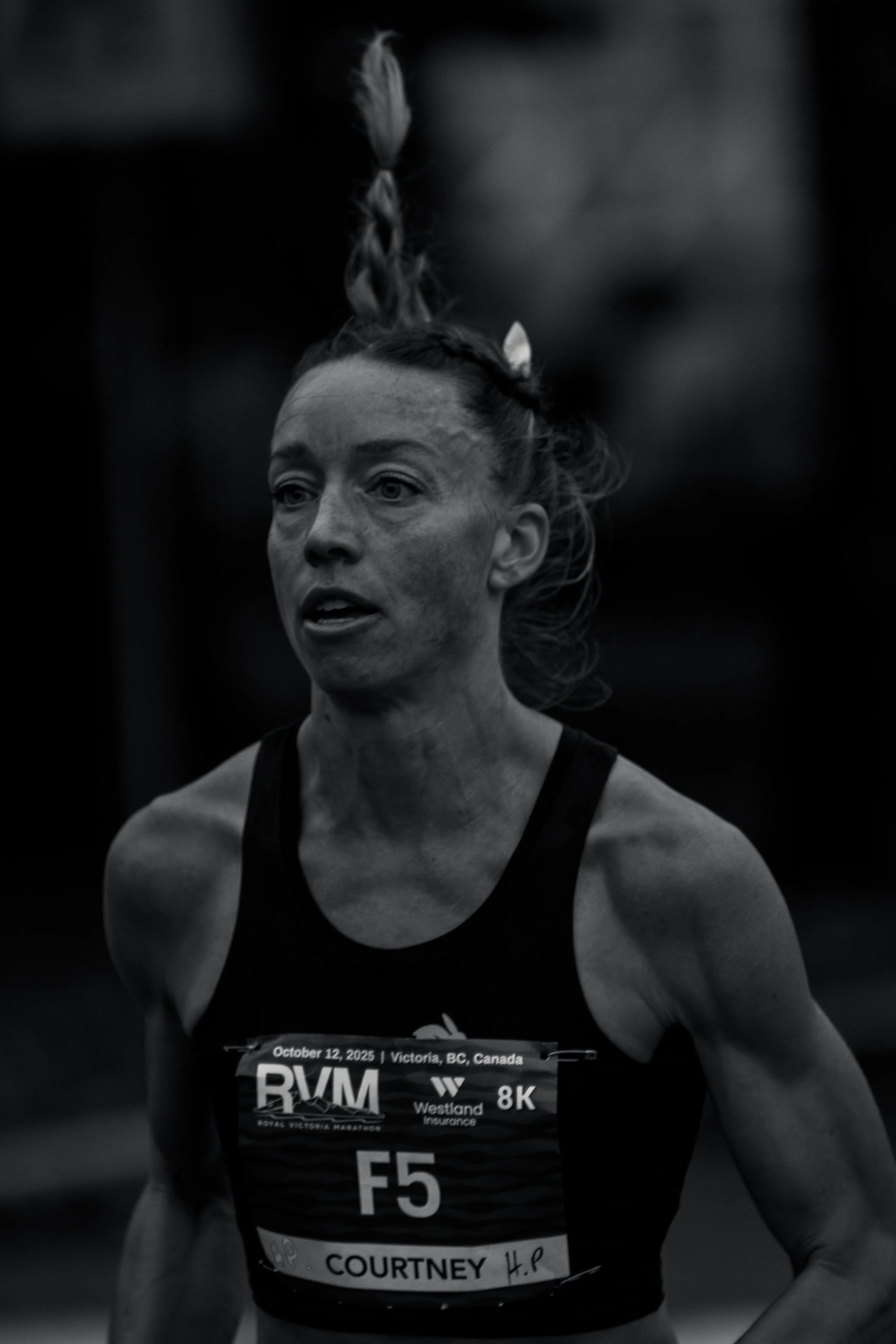 A female runner participating in a race, wearing a bib with her name 'Courtney' and race details, with dirt on her face and hair tied in braids.