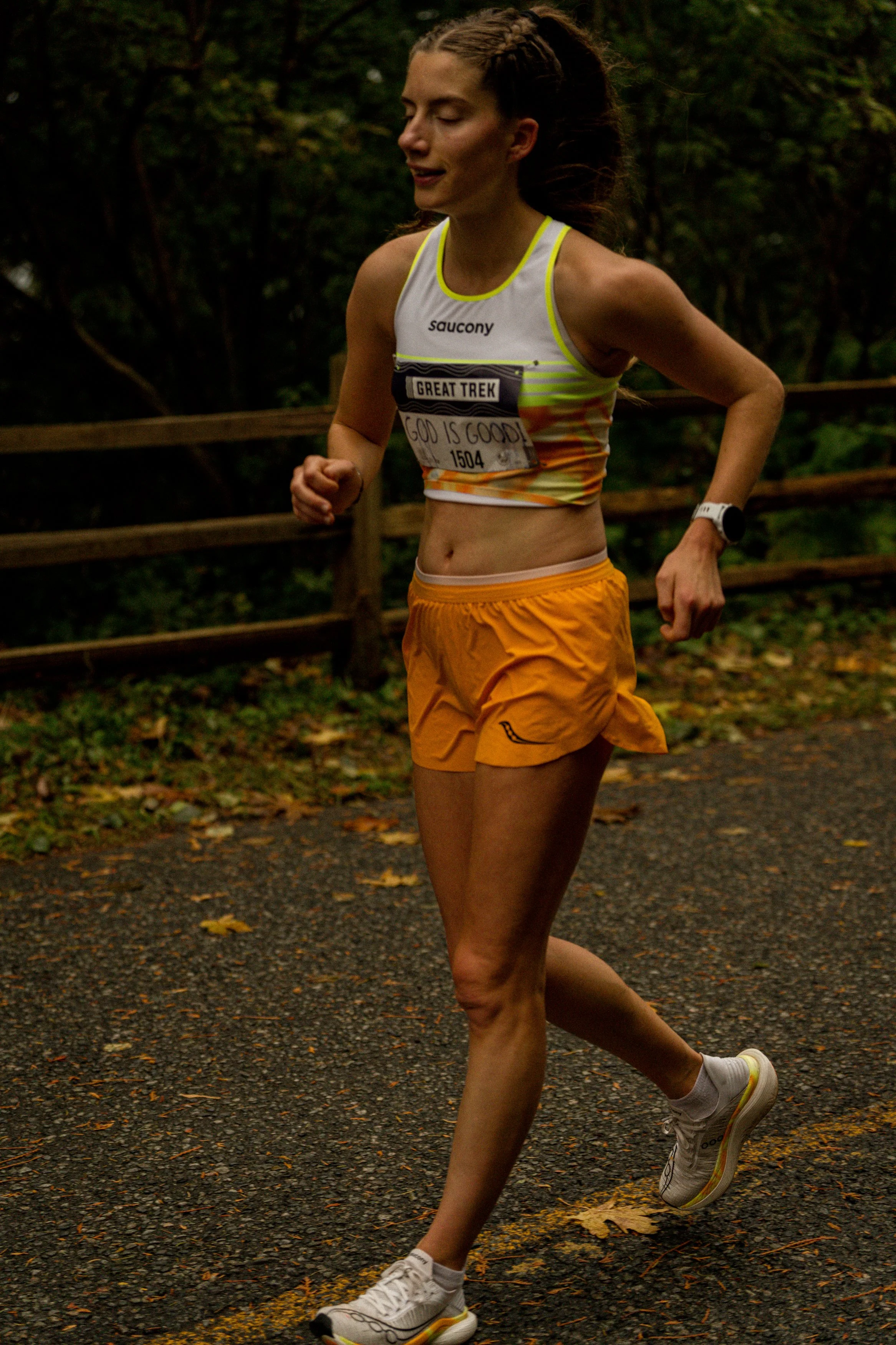 A female runner participating in a race on a gravel path in a wooded area with trees and leaves.