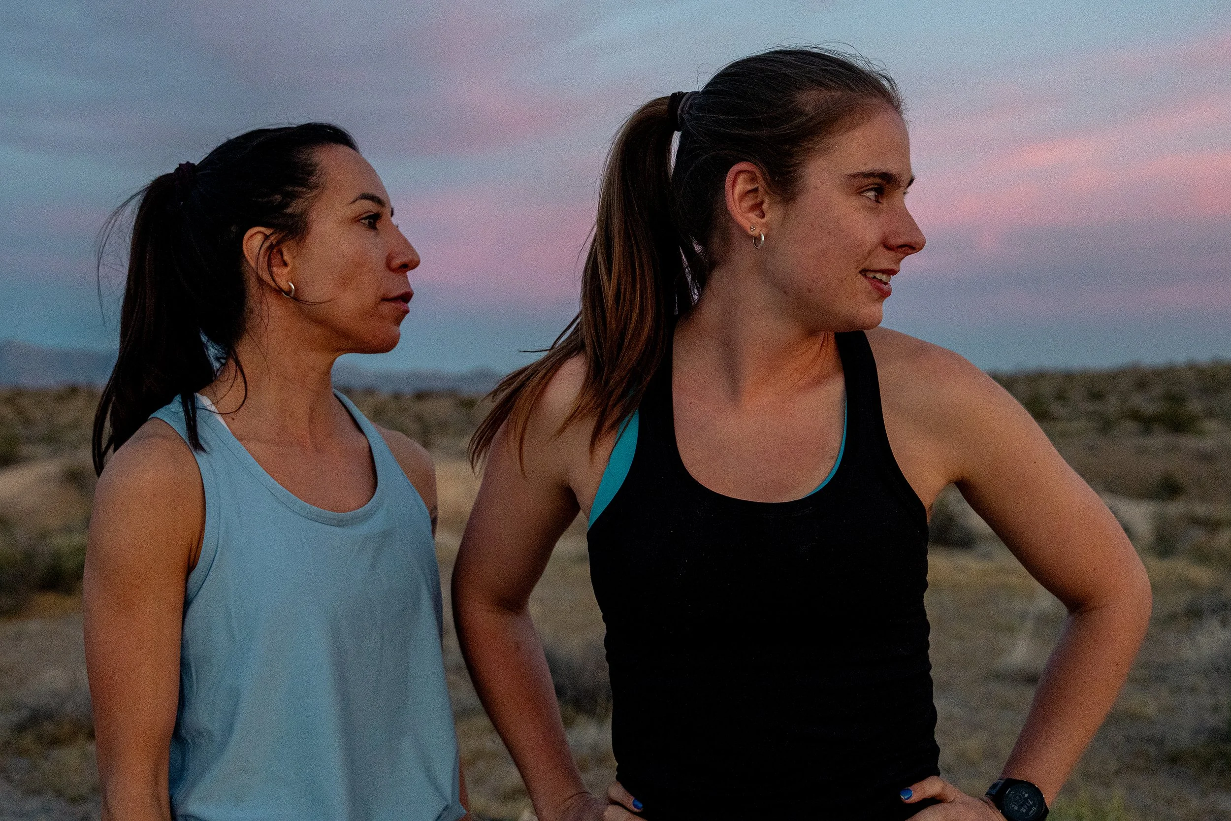 Two young women in athletic clothing standing outdoors at sunset with a landscape in the background.