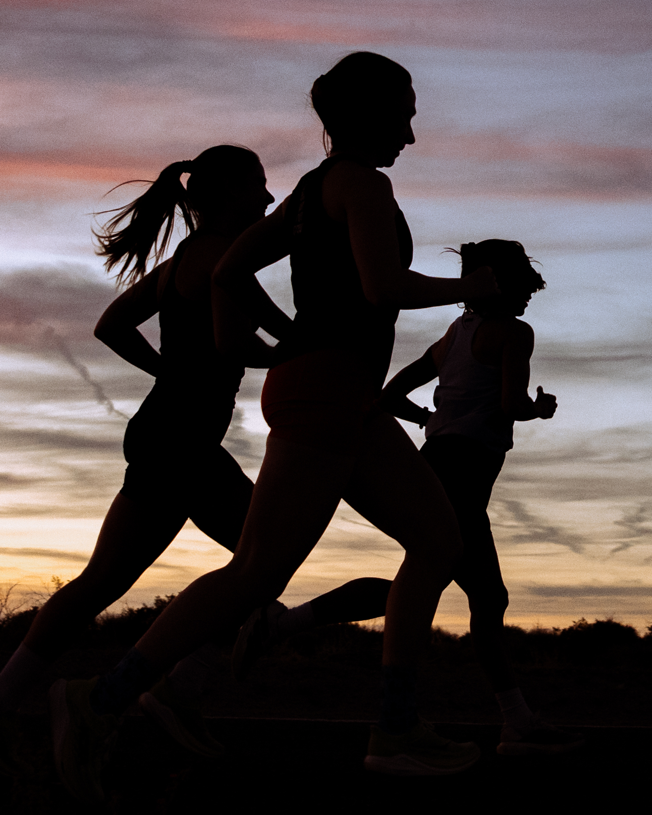 Silhouettes of four women running outdoors at sunset, with a colorful sky in the background.