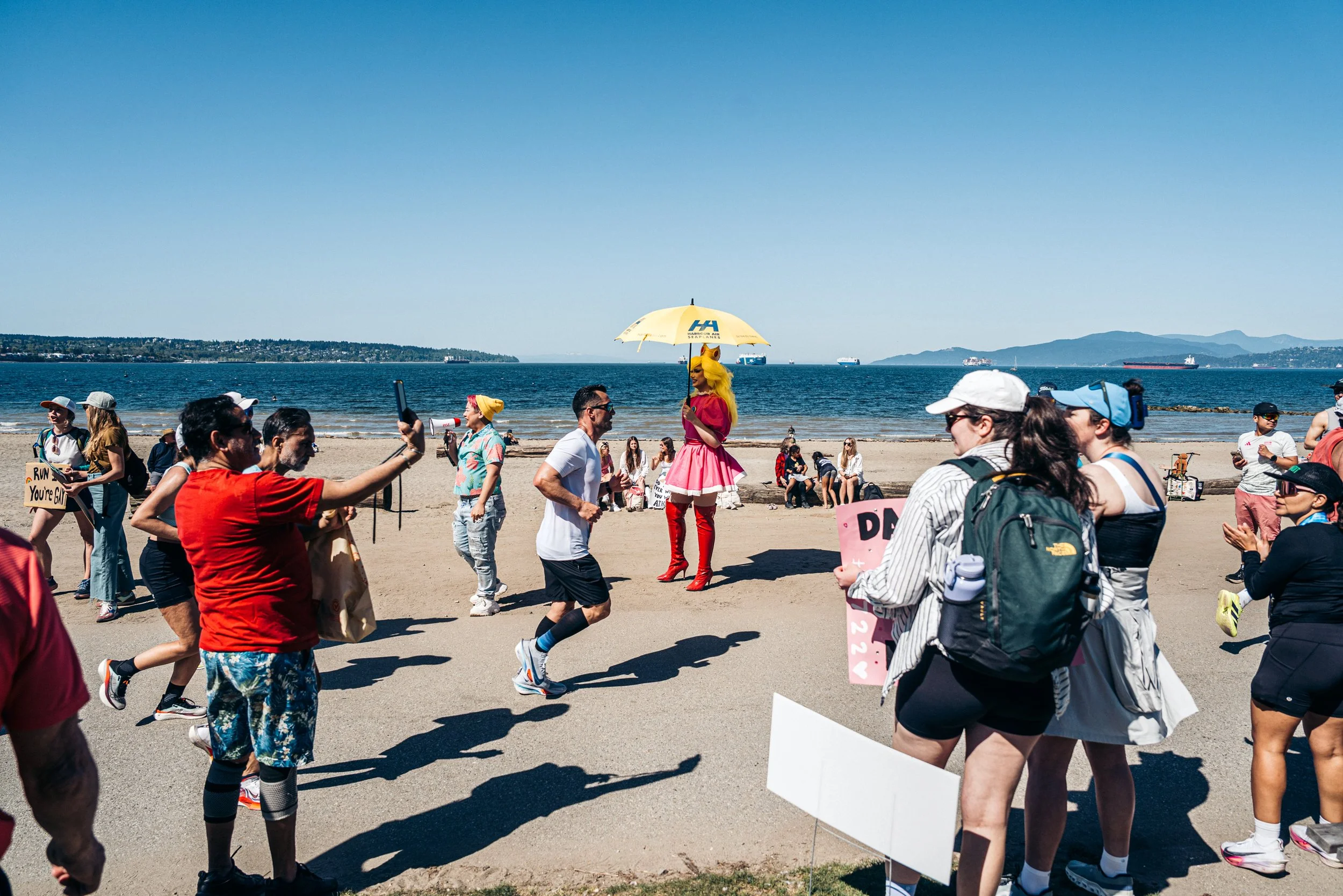 People participating in a protest march near the water, with a person dressed as a lion holding an umbrella and others holding signs.