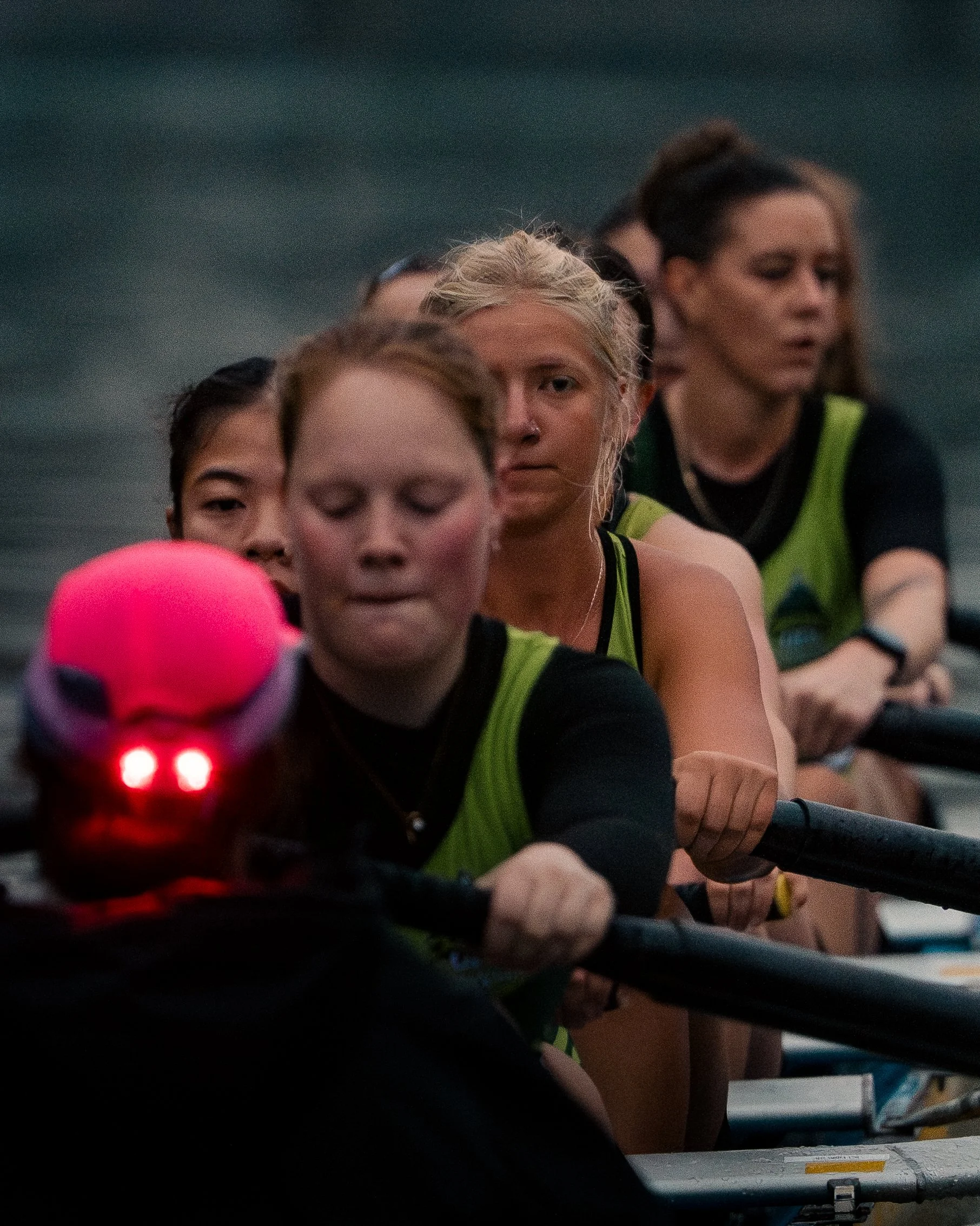 Female crew members wearing green life jackets paddling a dragon boat on a dark water body