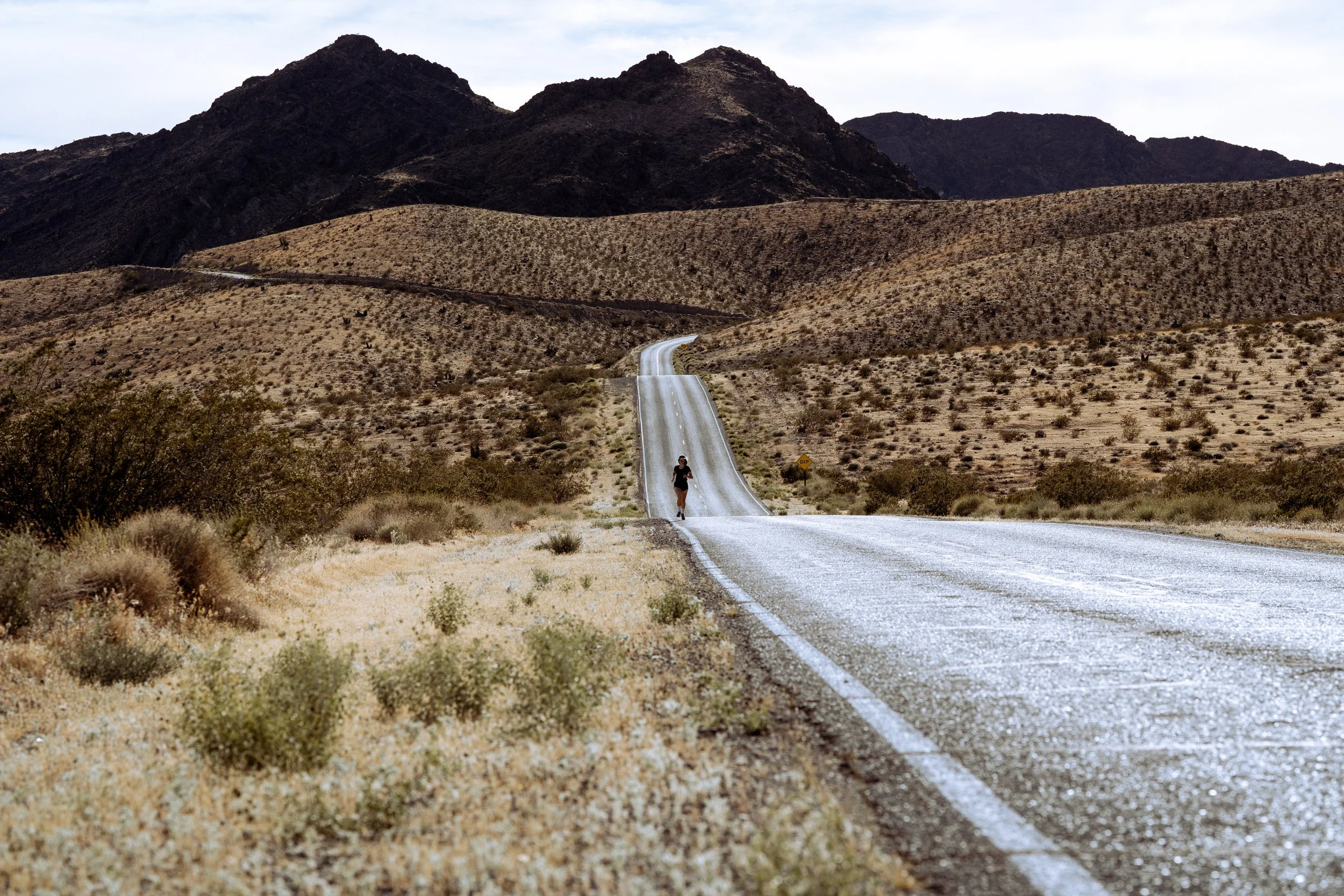 A person running on a long, winding road through a desert landscape with mountains in the background.