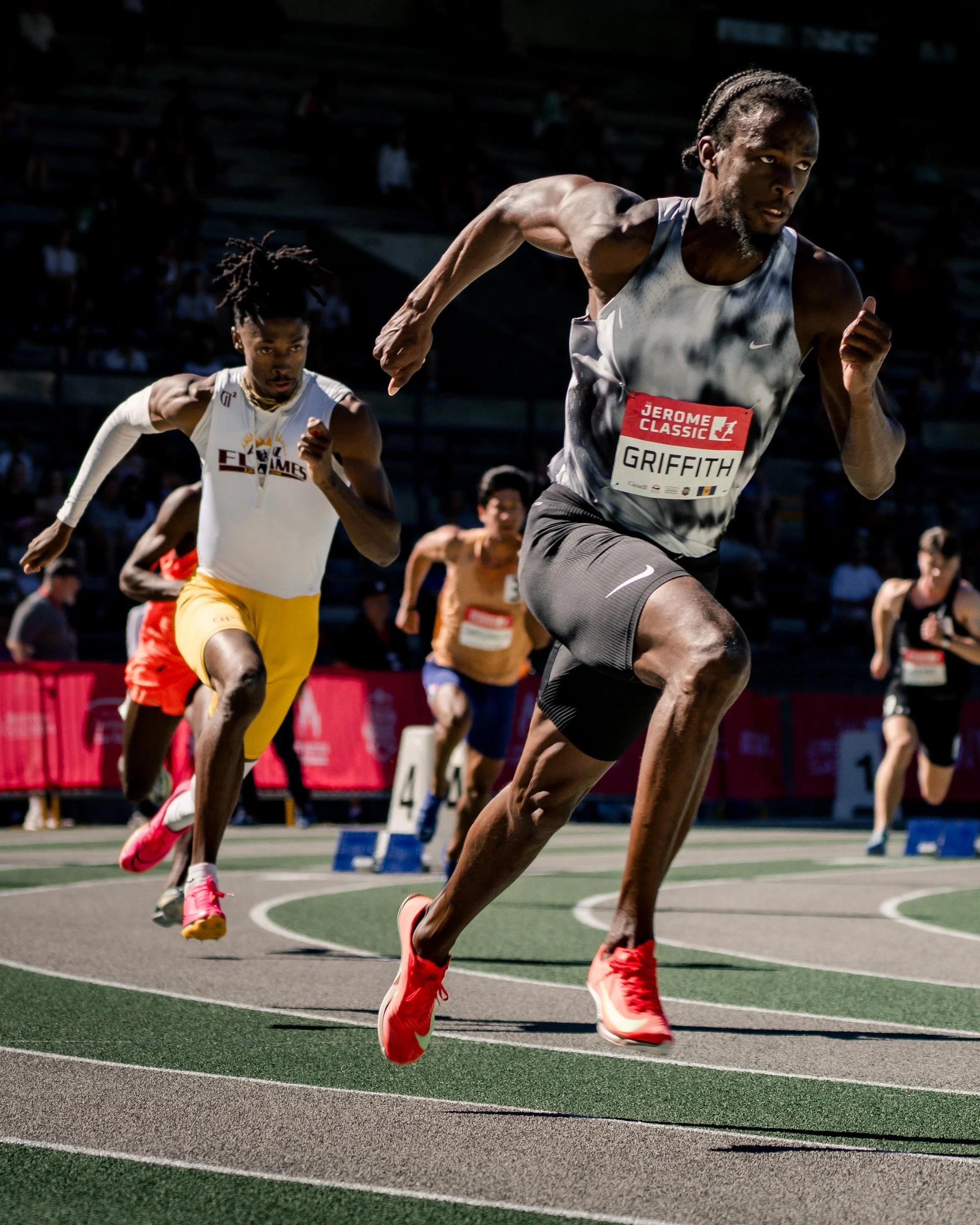 Track athletes running in a race on a stadium track with spectators in the background.