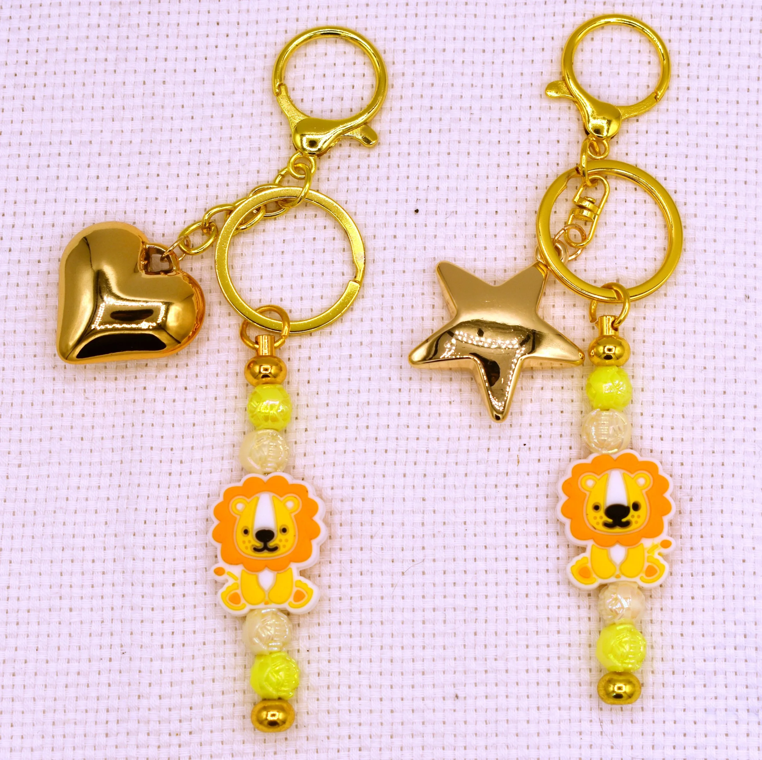 Close-up of a yellow and gold beaded jewelry set with heart, star, and lion charms on a pink textured background.