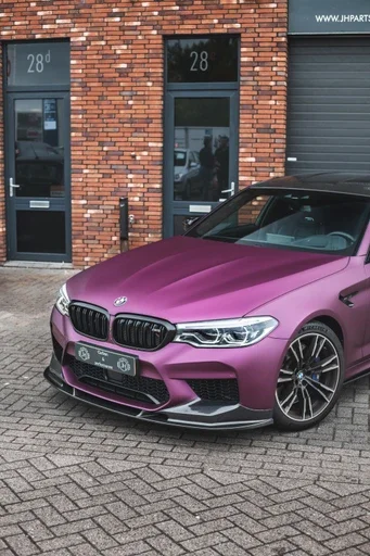 A matte purple BMW parked outside a brick building with large glass doors and windows.