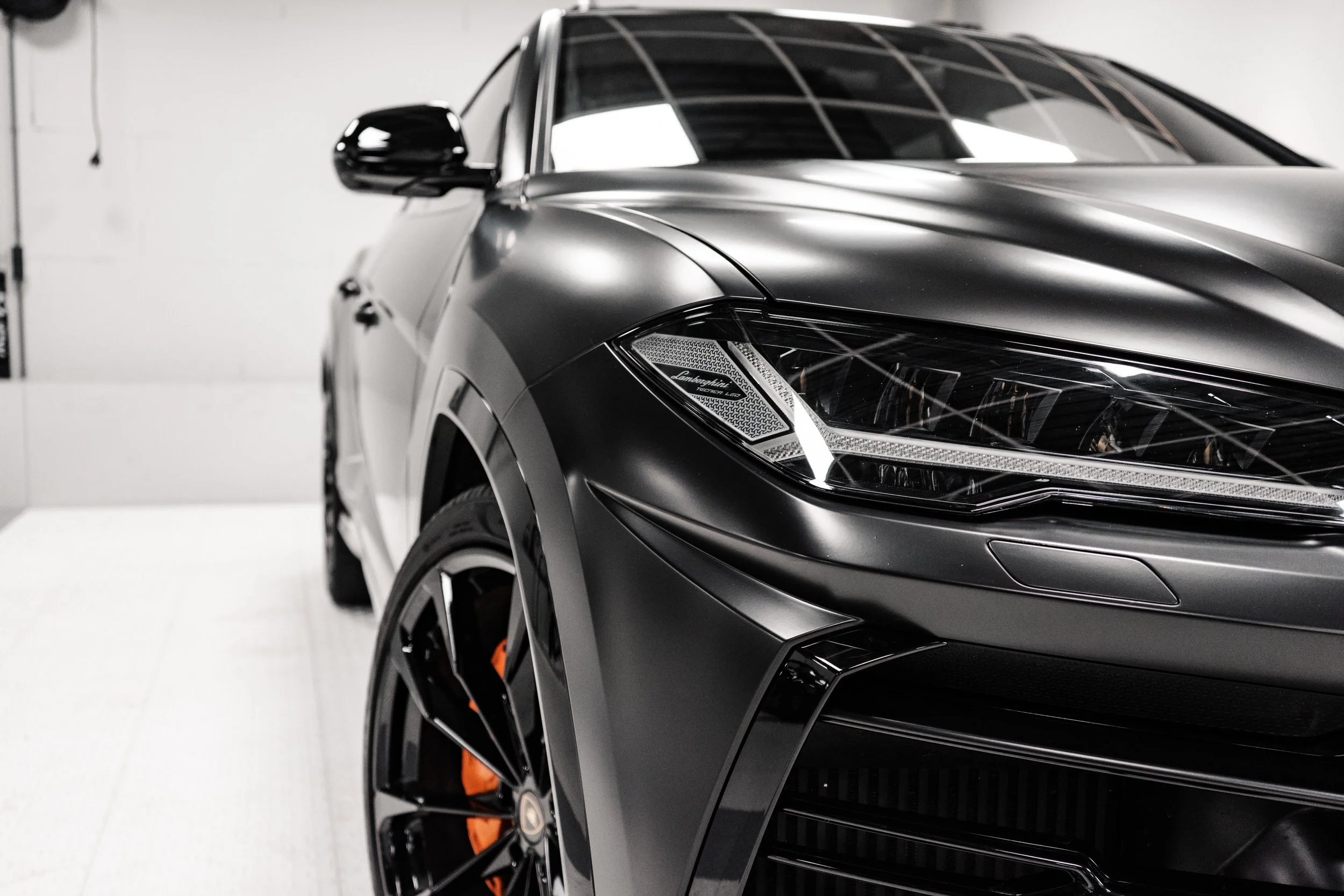 Close-up of a sleek, black luxury sports car with sharp headlights and orange brake calipers, parked indoors.