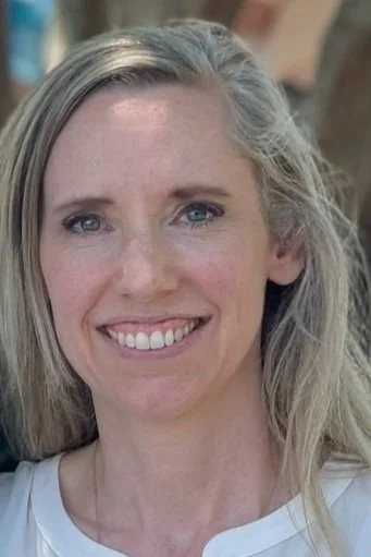 Close-up of a smiling woman with blonde hair and blue eyes, wearing a white top.
