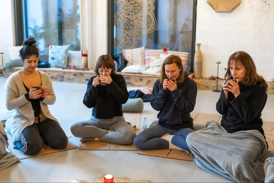 Circle of women drinking ceremonial cacao in calm room filled with lights