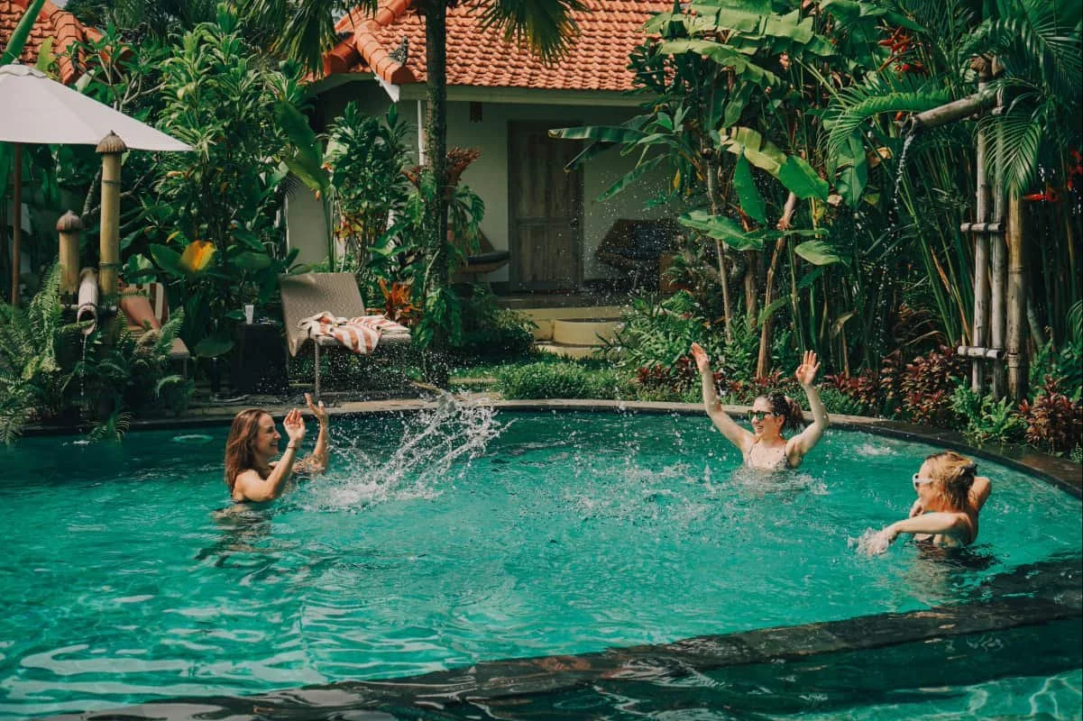 Three women are splashing in private pool with exotic plants around them in Bali