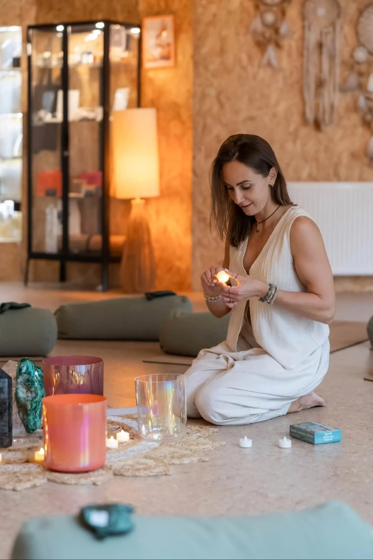 Woman is lighting a candle in a circle of bolsters eye masks crystals
