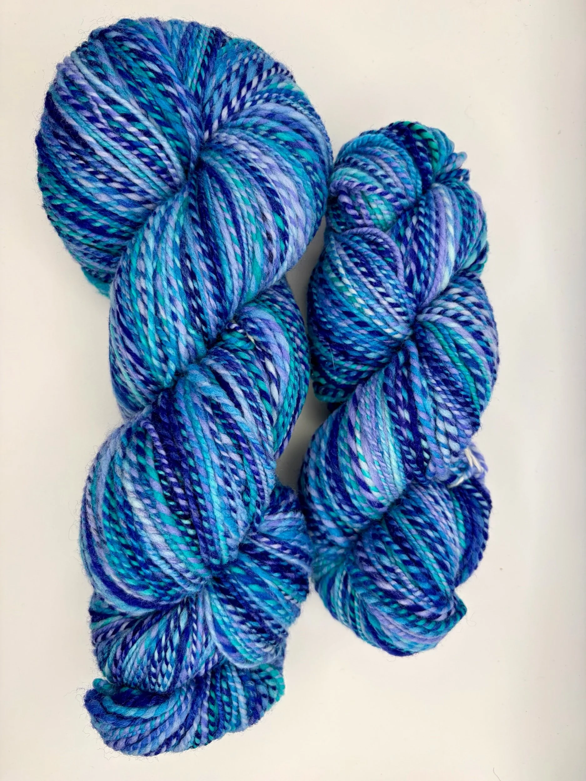 2 skeins of handspun yarn in shades of blue, purple, and turquoise