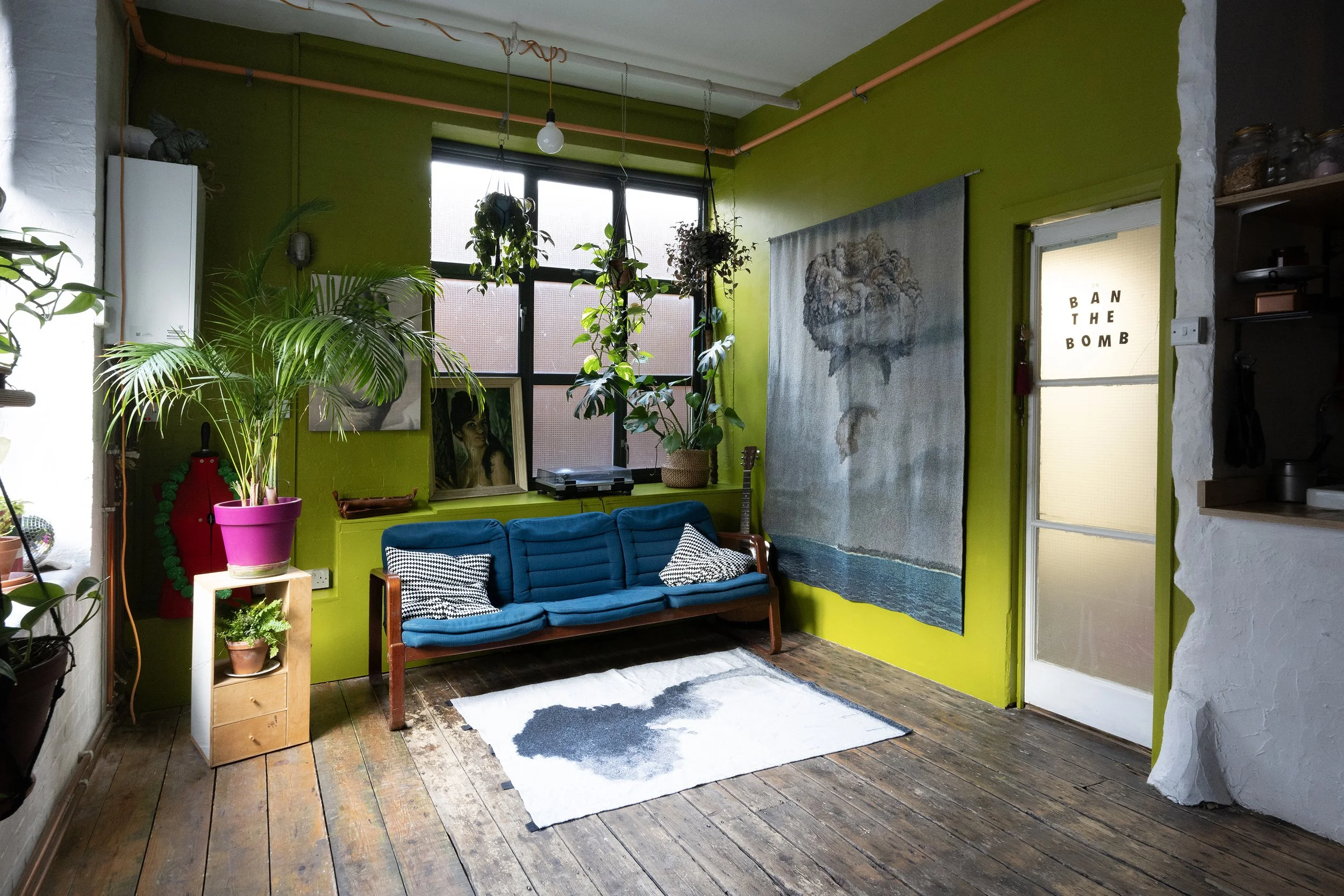 Living room with a passionate olive green wall, Danish style sofa and hanging plants all around.