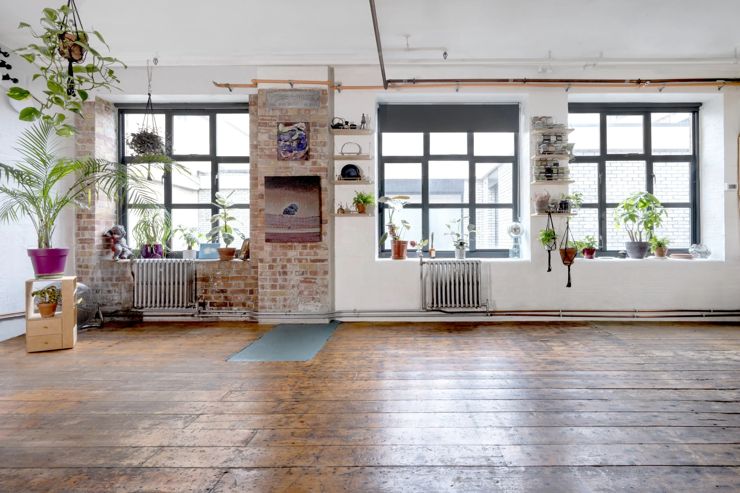 A bright, airy room with large windows, potted plants, a brick wall, and wooden floors.