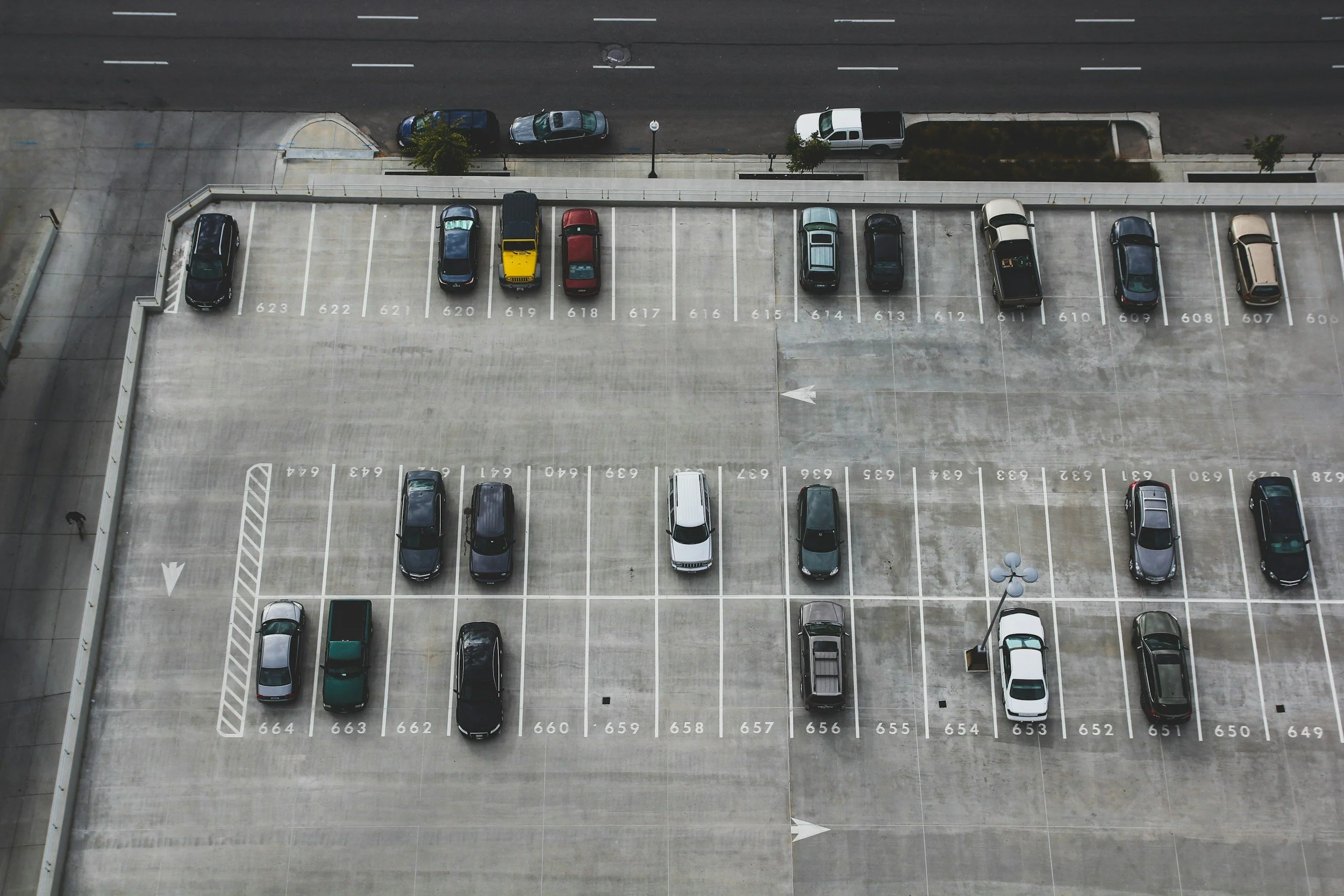 Empty rooftop parking lot with cars parked in numbered spaces and a few cars parked along the street.
