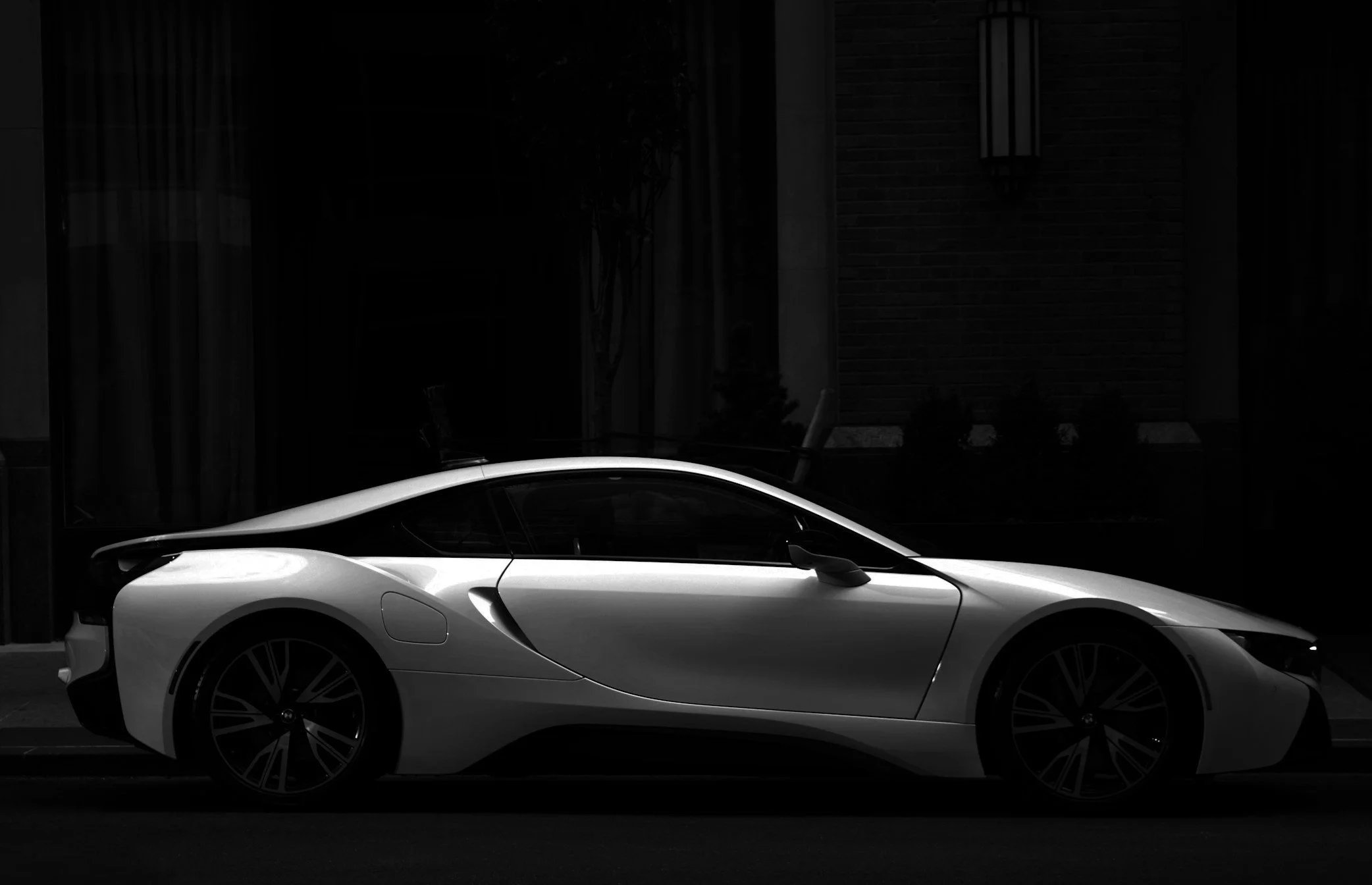 A sleek white sports car parked on a dark street at night, with a brick building and street lamp in the background.