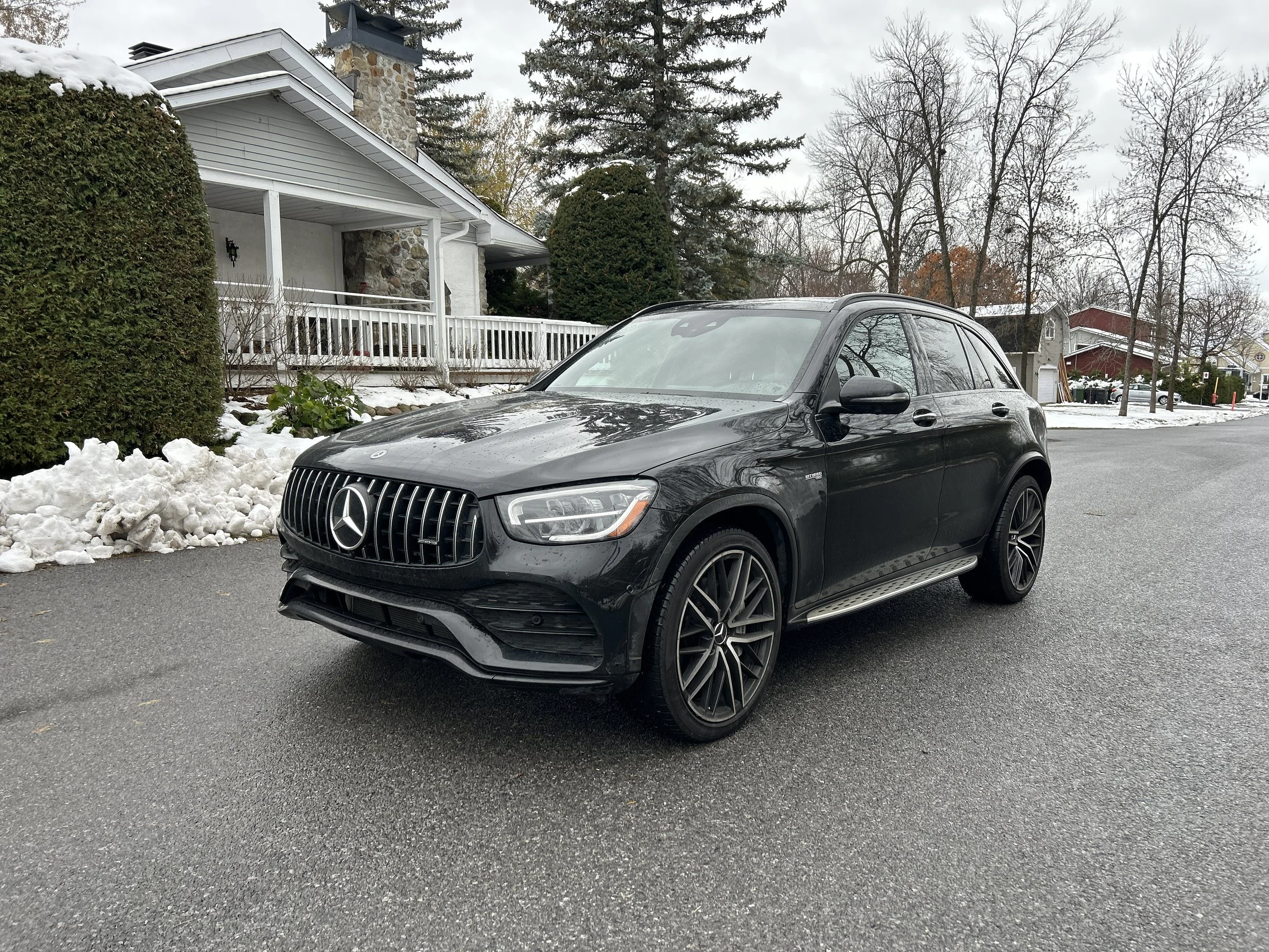 Black Mercedes-Benz SUV parked on a residential street with snow on the ground and houses in the background.