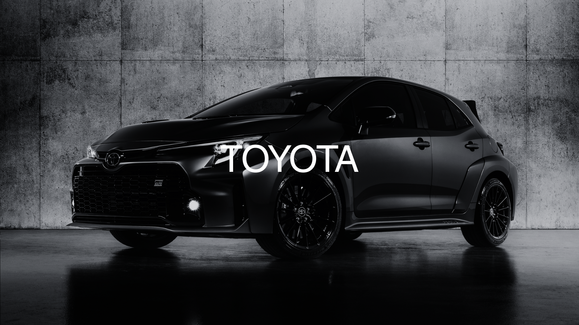 A black Toyota car parked on a concrete floor against a concrete wall background