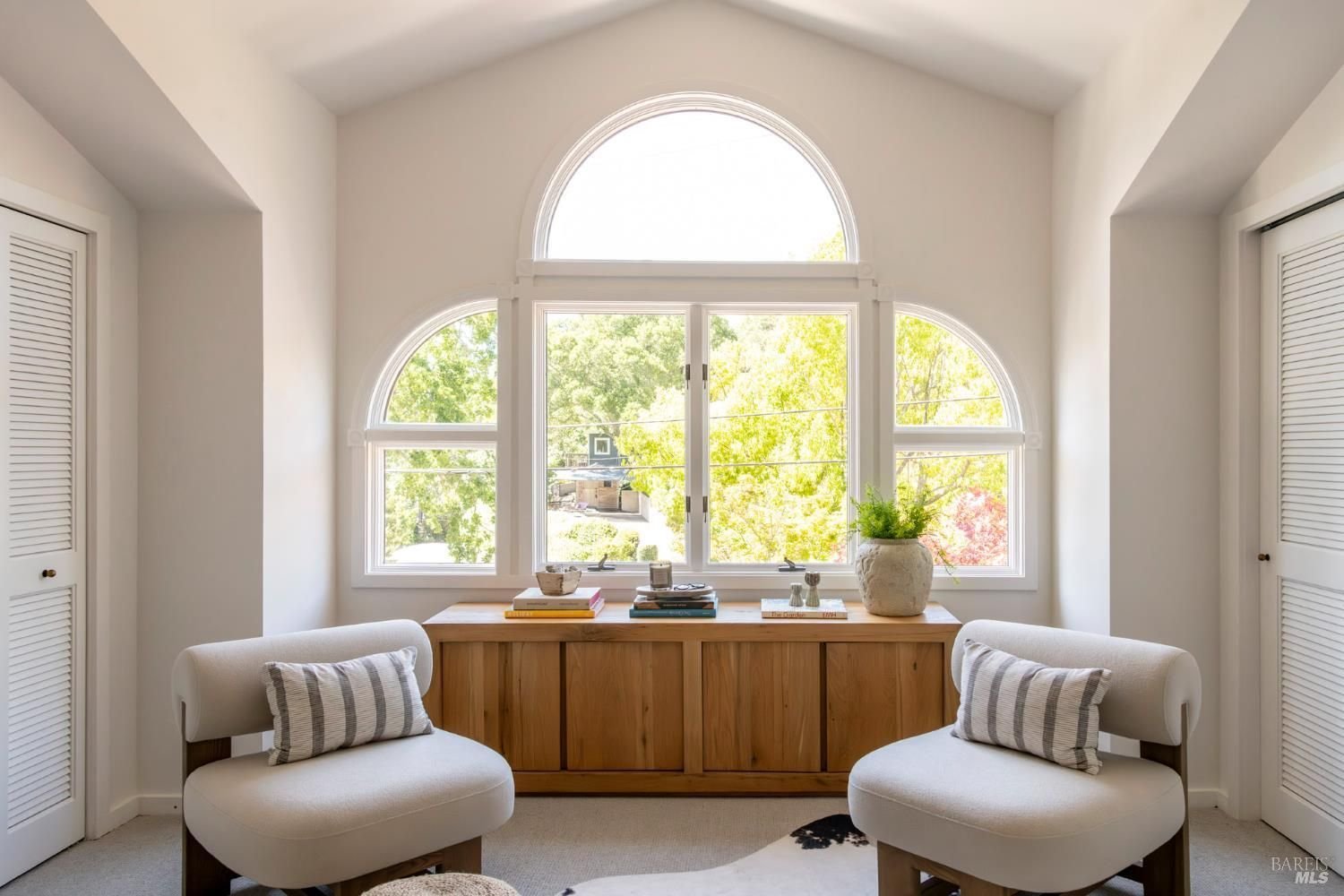 Living room with a fireplace, cream sofa, and built-in shelves, viewed from the dining area with a wooden table and chairs. Modern decor with plants, artwork, and wooden accents.