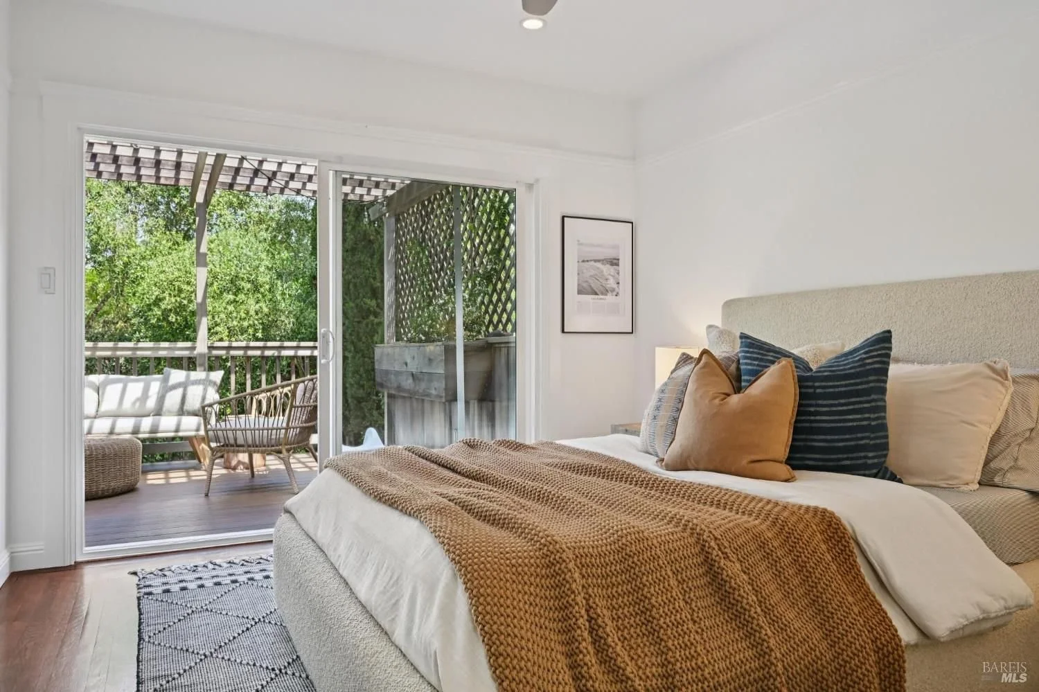 Living room with large glass doors leading to outdoor patio, wooden sliding barn door, desk with laptop, mirror, and decor, with outdoor furniture and garden visible outside.
