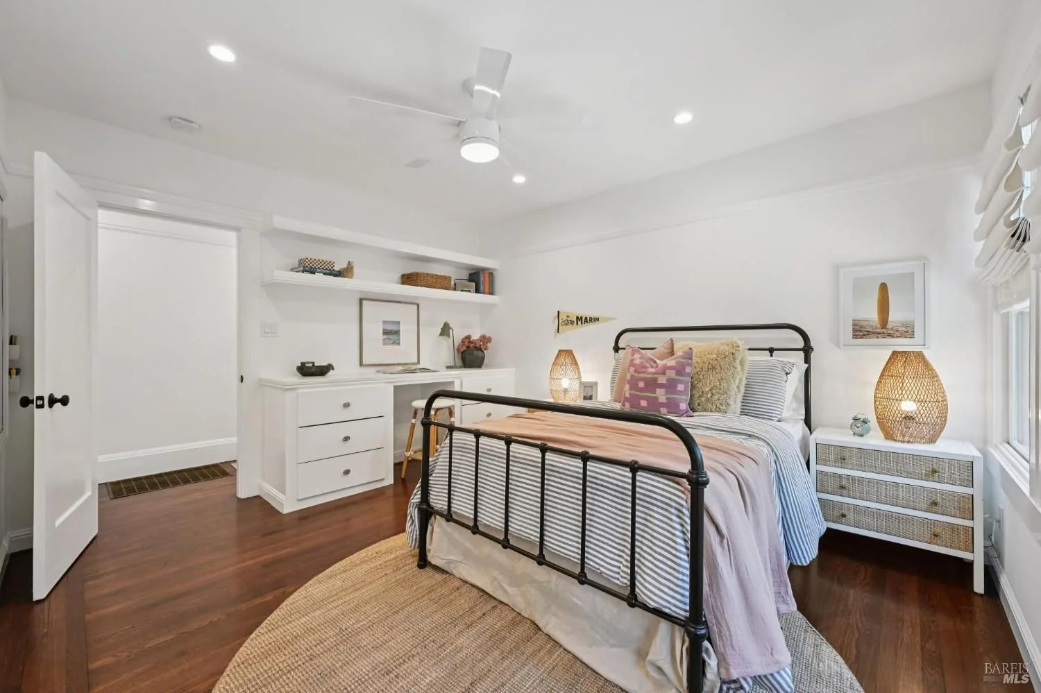 Modern dining area with a white table and six black chairs, open to a kitchen with white upper cabinets, dark lower cabinets, a stainless steel range hood, white subway tile backsplash, and a large potted plant centerpiece on the table.