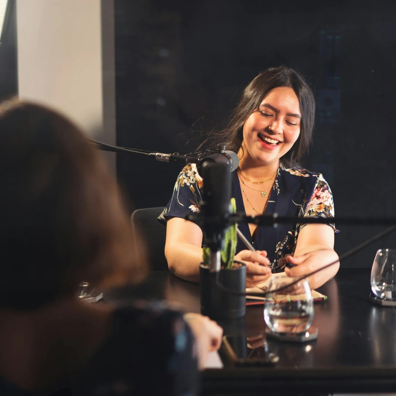 A modern, minimalist house with wooden and stone elements situated on green rolling hills, with a backdrop of snow-capped mountain peaks and a cloudy sky.