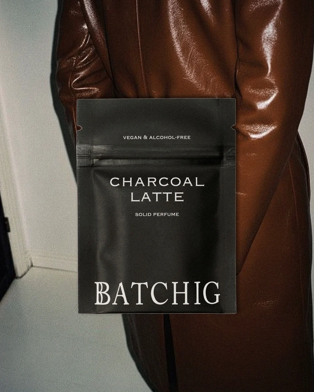 Charcoal Latte solid perfume by Batchig – black packaging pouch against brown leather coat, Coffee Break trend by WSSC