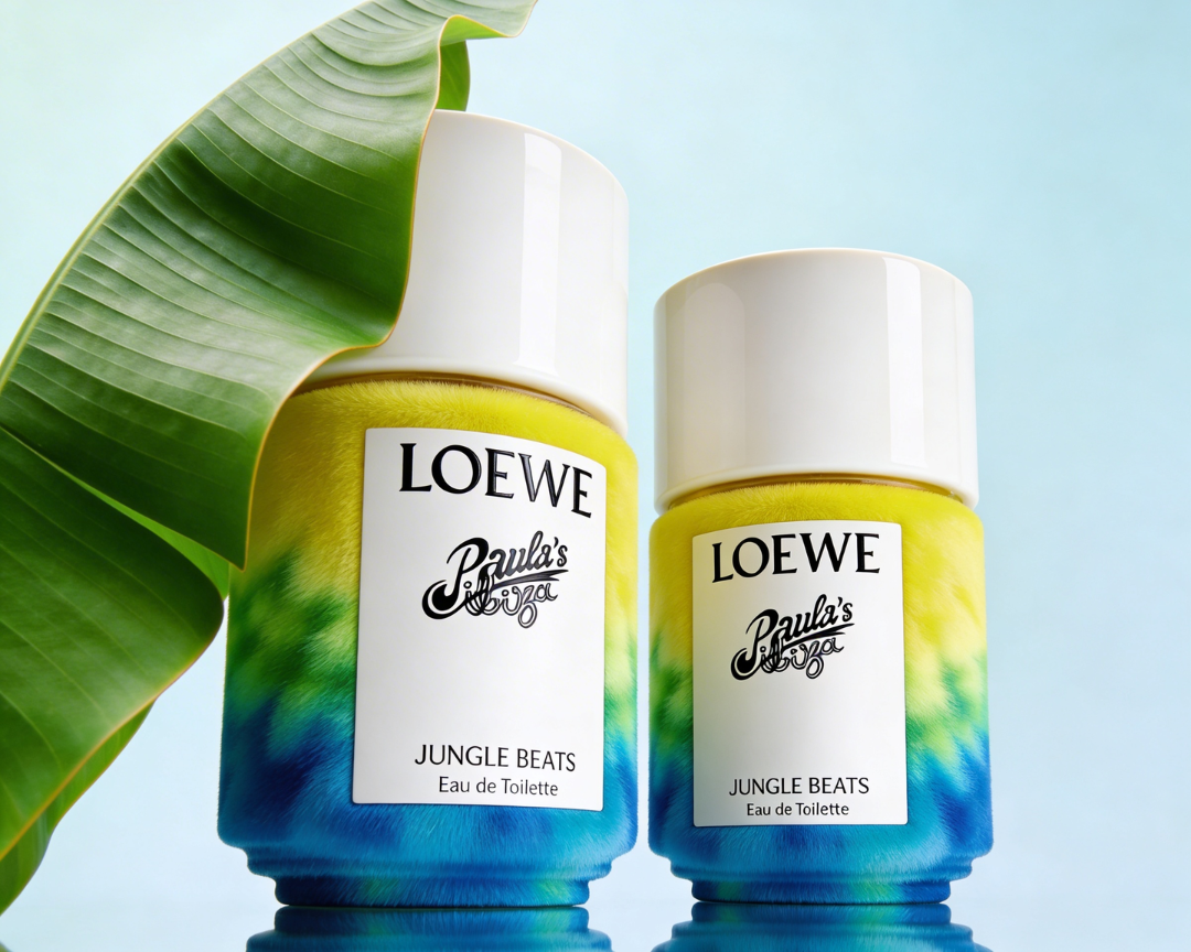 Two bottles of LOEWE Paula's IBIZA Jungle Beats Eau de Toilette, with a large green leaf draping over the larger bottle, against a light blue background.