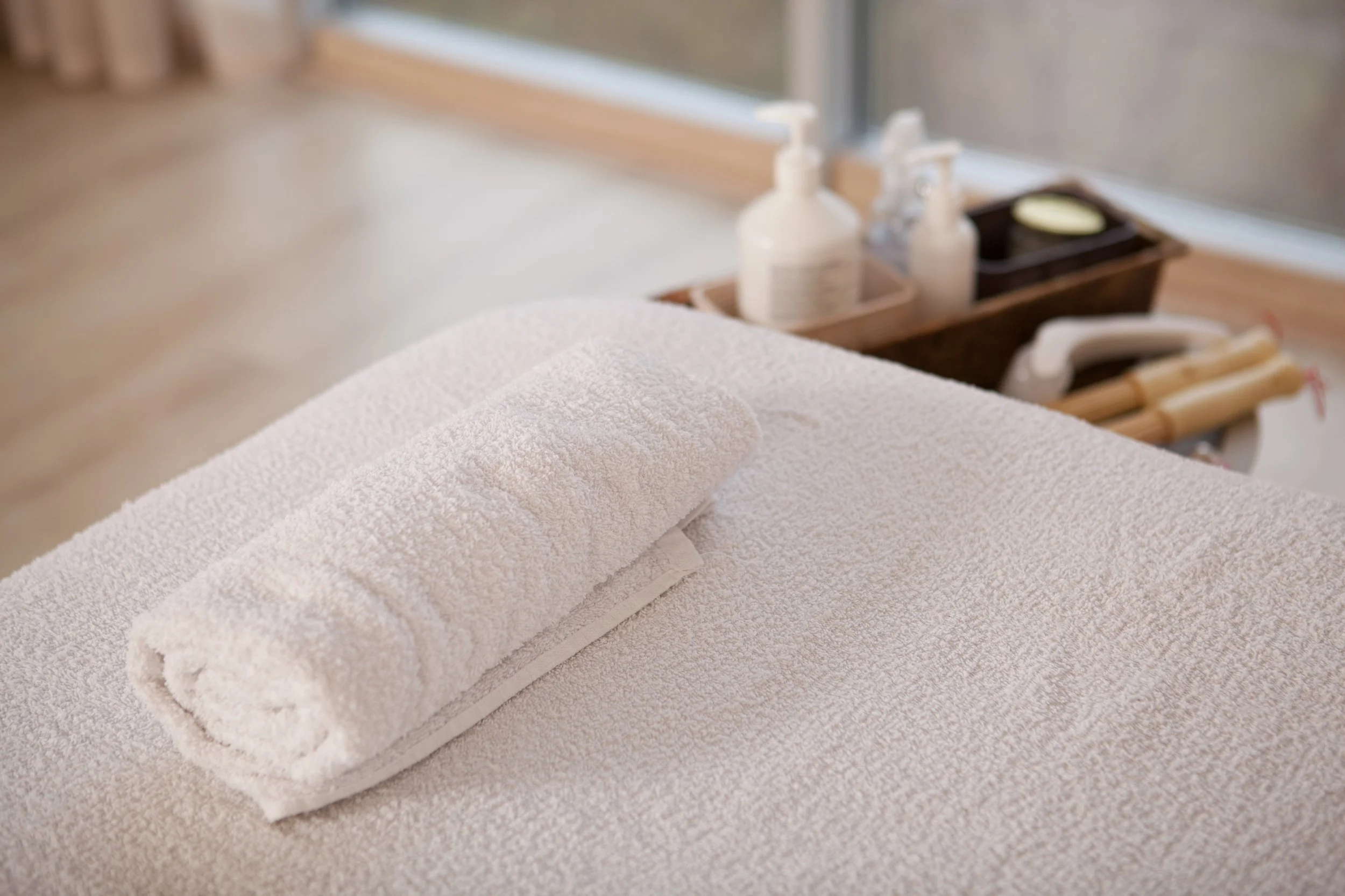 A rolled white towel placed on top of a folded towel on a table, with soap and lotion bottles in the background.