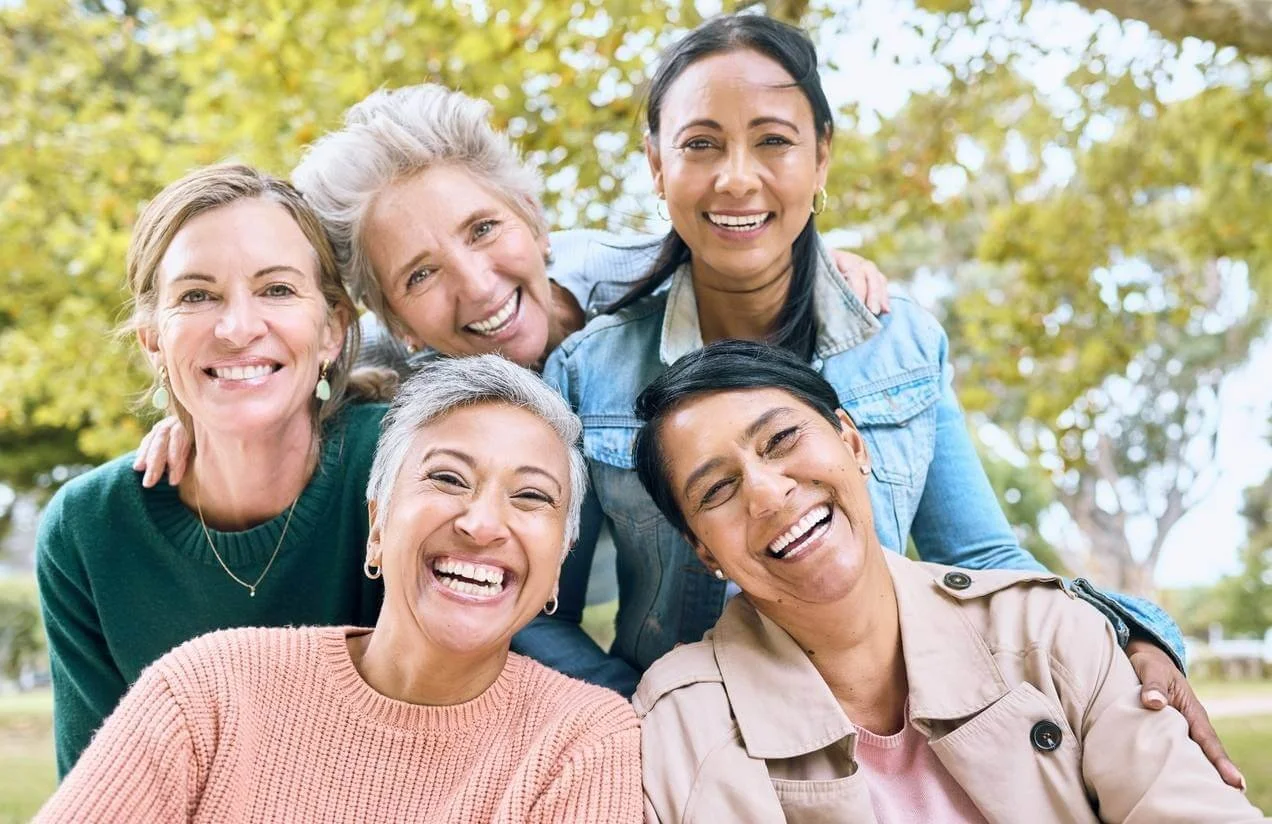 Group of five women smiling outdoors, standing close together.