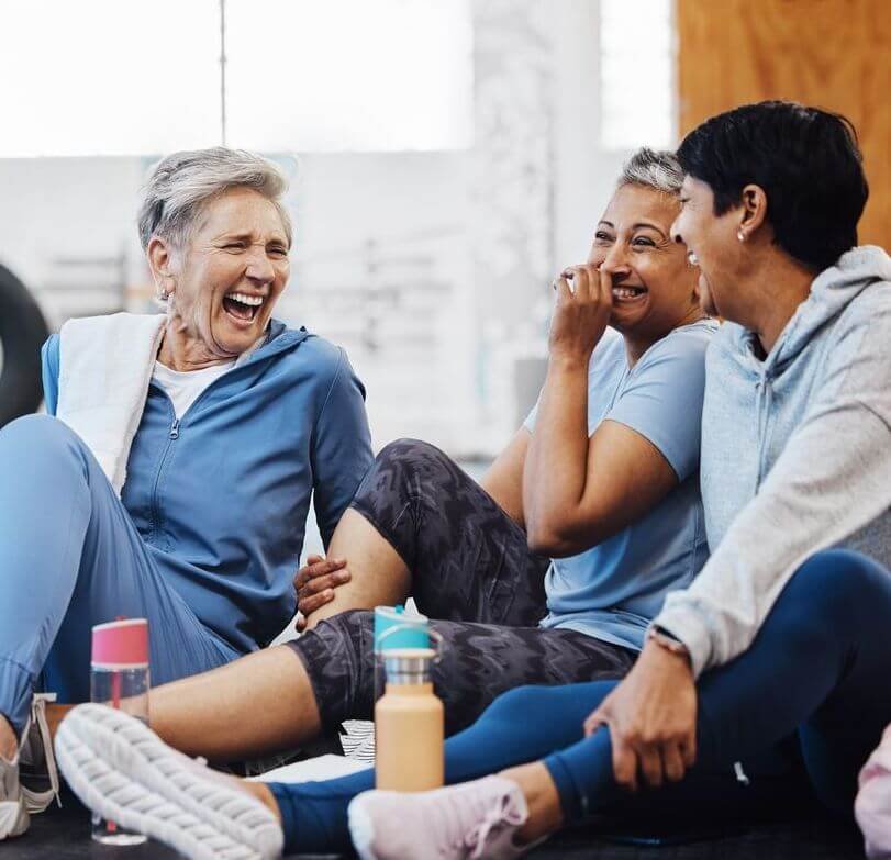 Three women laughing and sitting on the floor during a workout session.