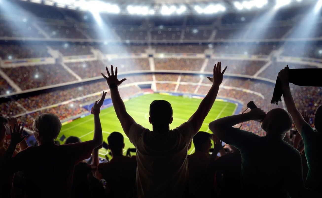 Crowd of people watching a sports game in a stadium with bright lights.