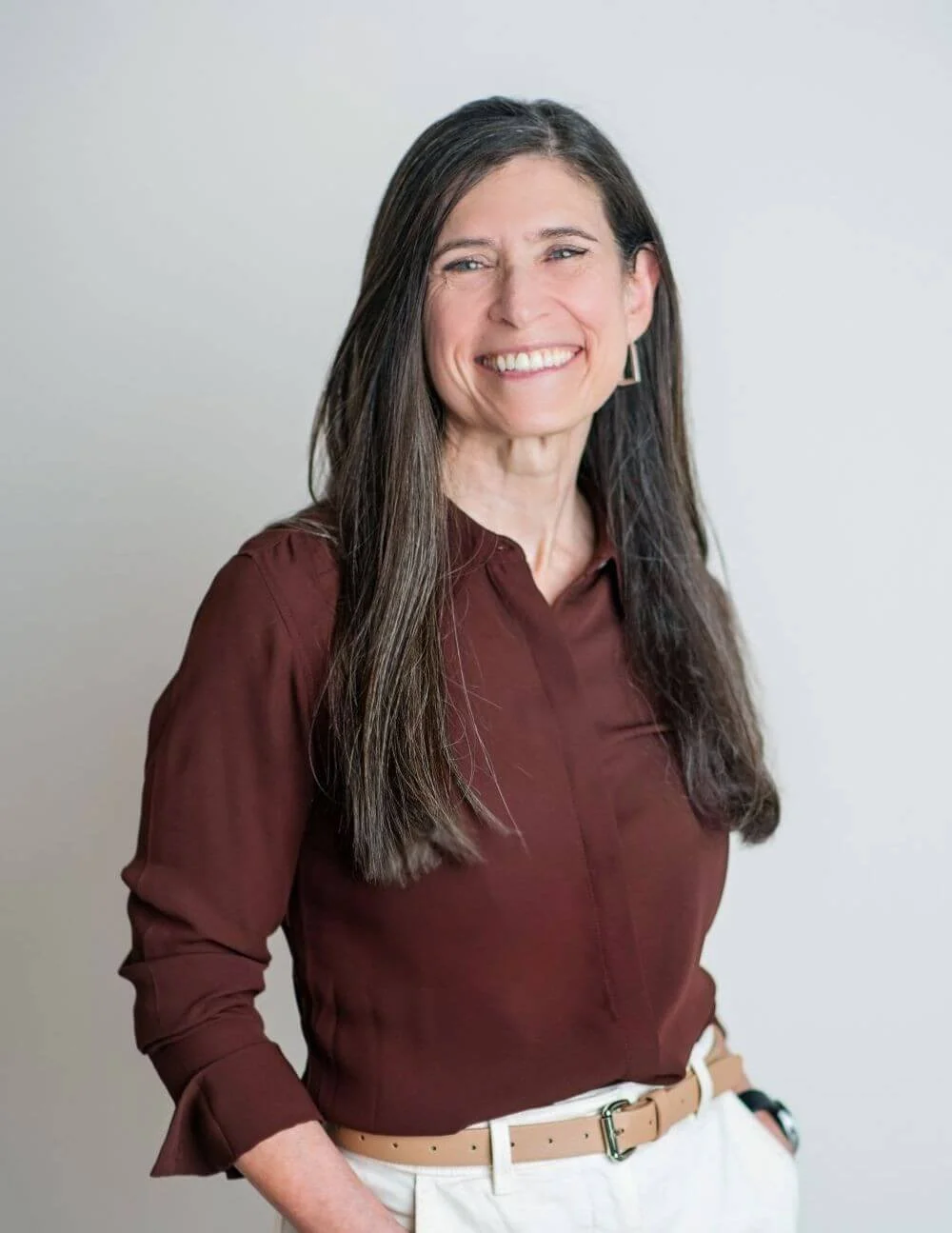 Dr. Thoman, smiling and wearing a maroon shirt and white pants, standing against a plain light background.