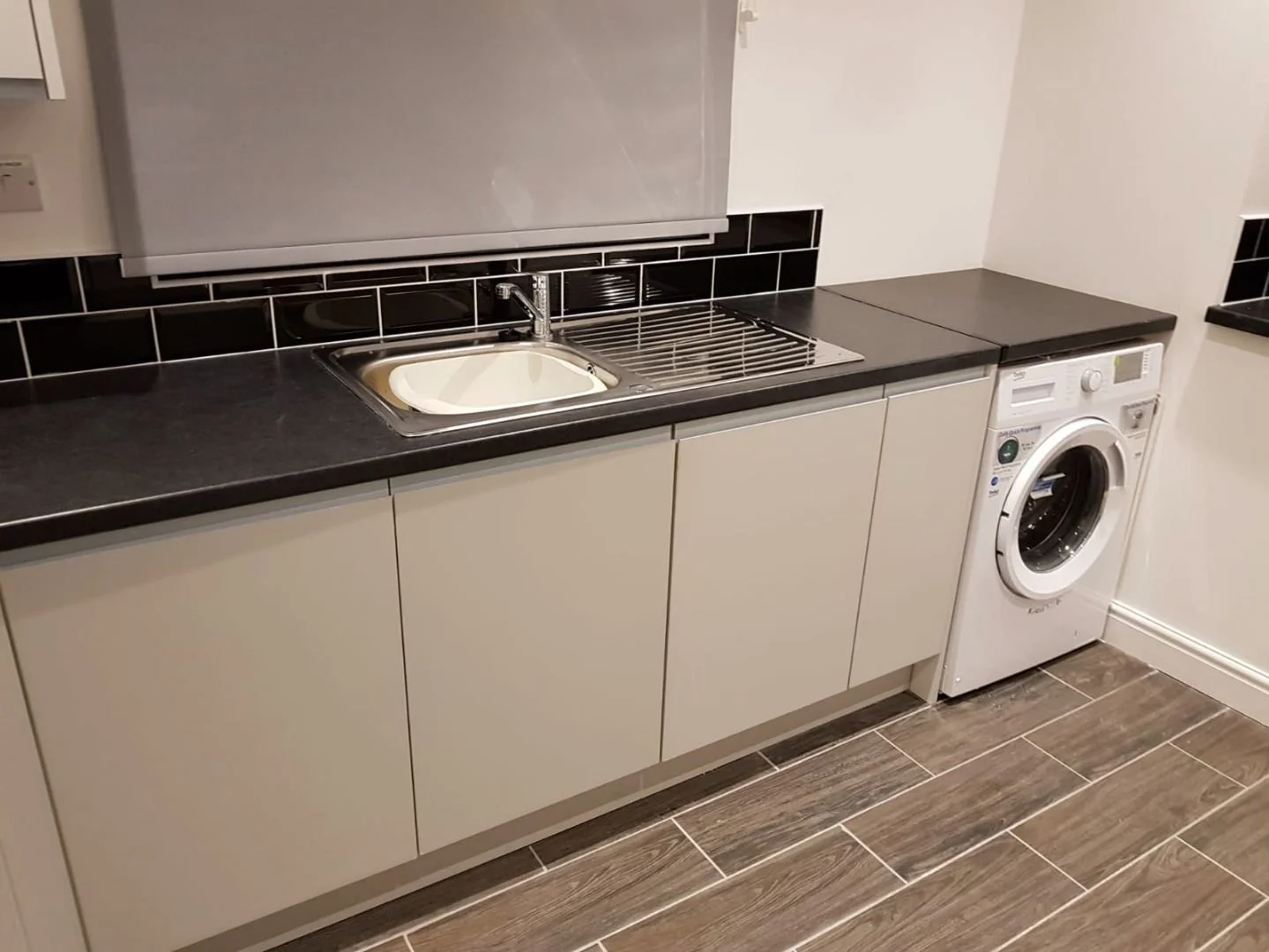 Kitchen with a black countertop, beige cabinets, stainless steel sink, black-tile backsplash, and a washing machine.